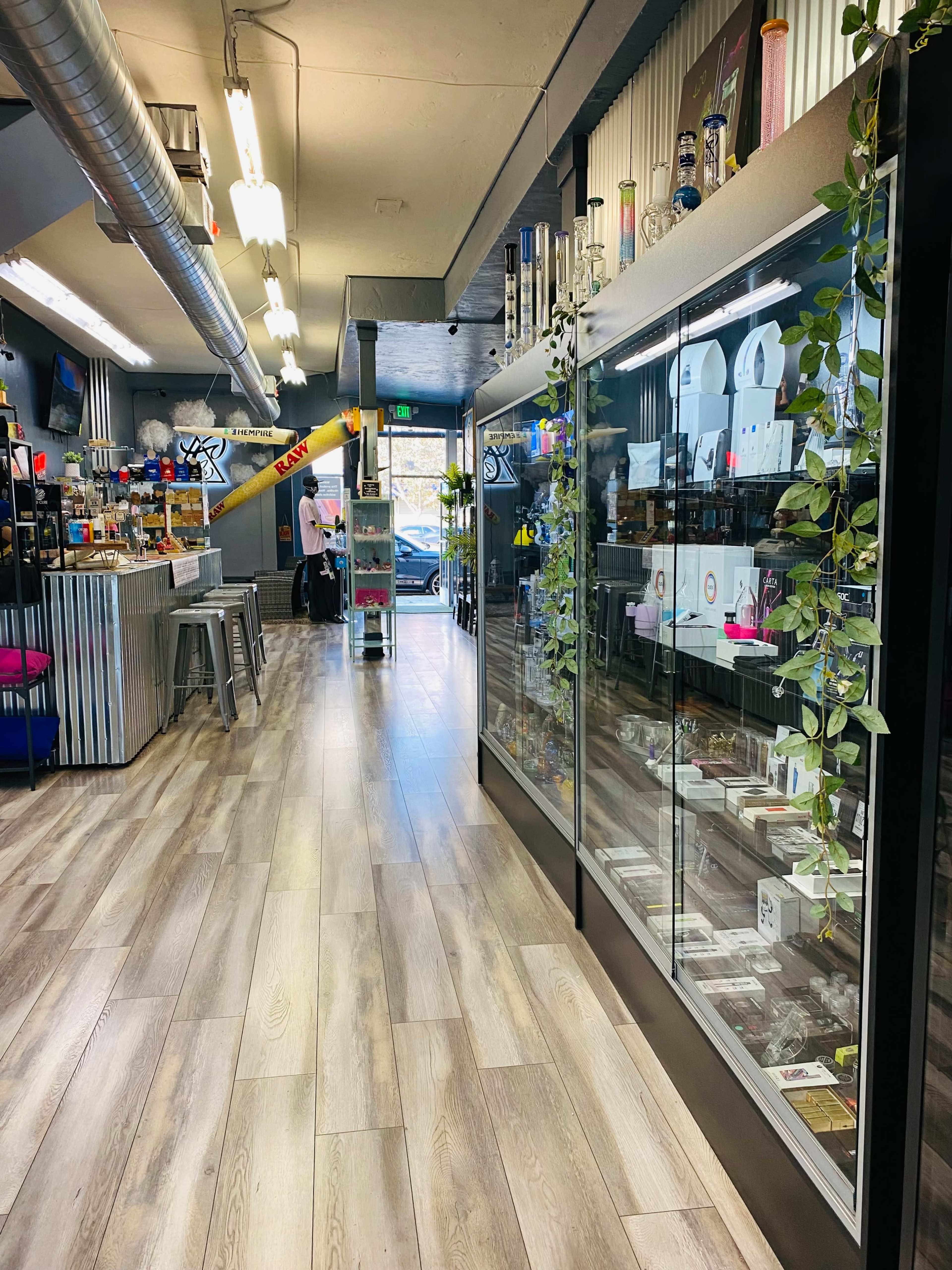 The interior of a retail store features glass display cases on the left side and a view of the entrance at the far end, with shelves stocked with various products.