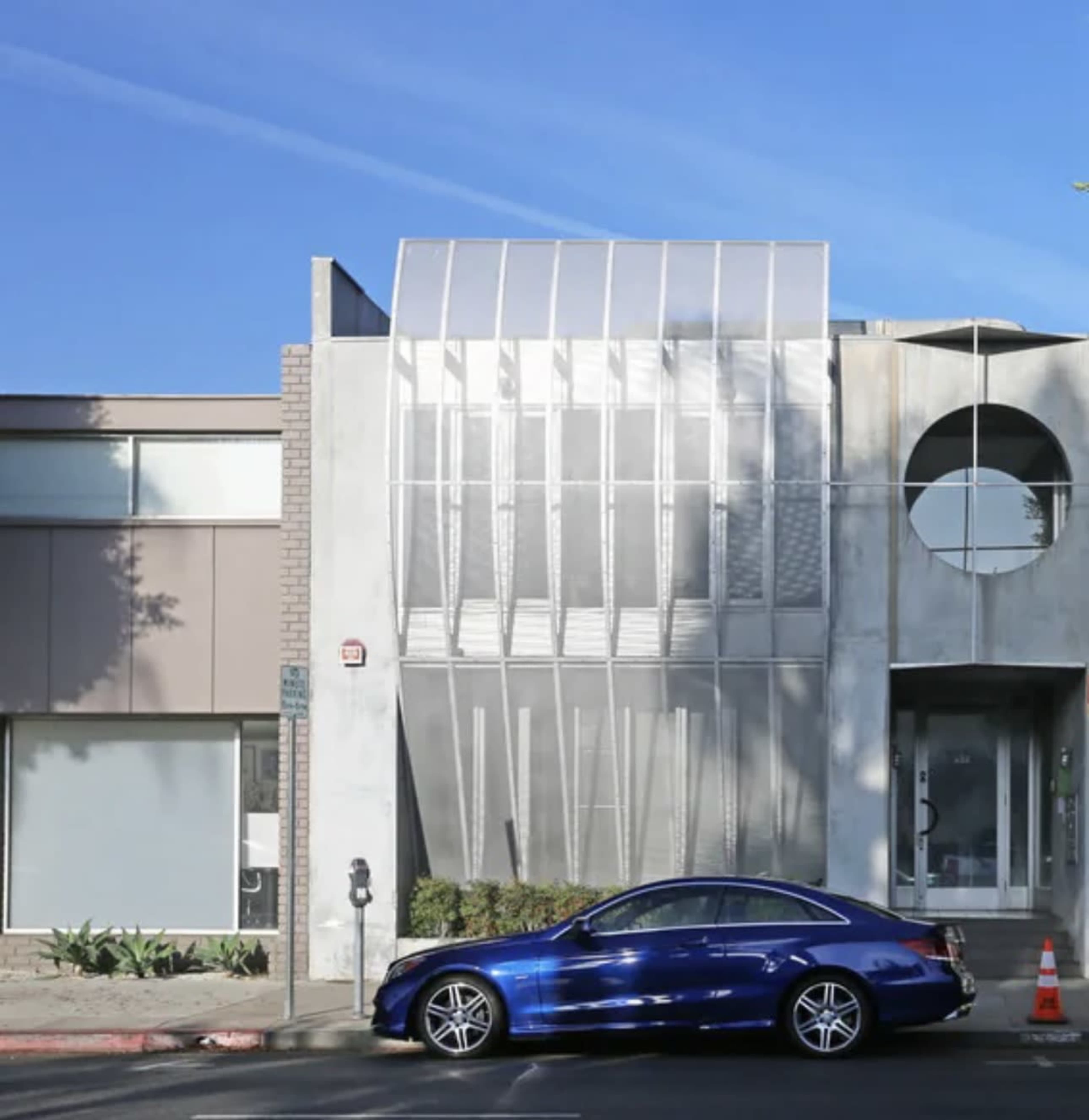 A modern building features a combination of sleek materials and geometric shapes, with a blue car parked in front.