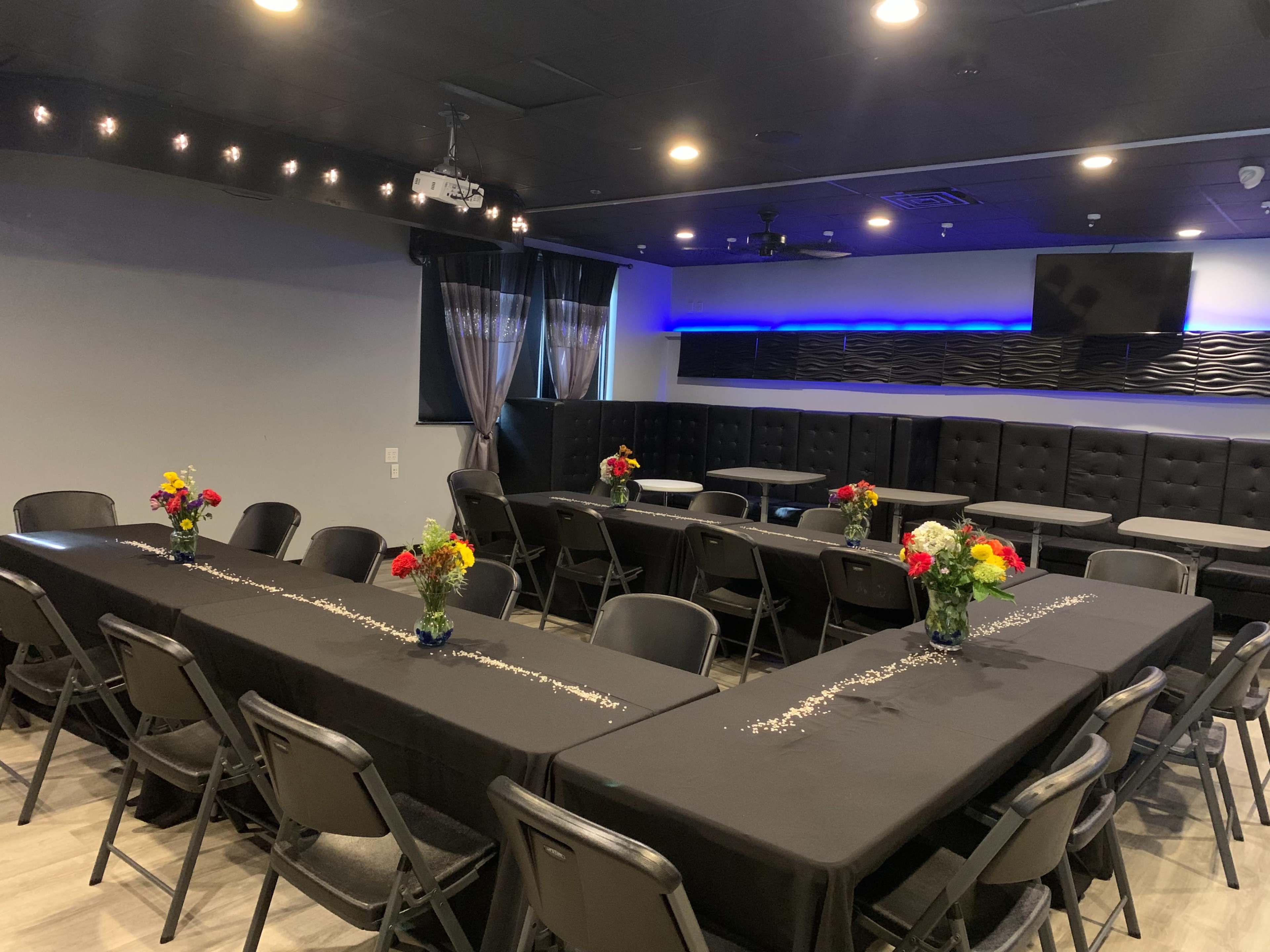 A well-arranged meeting space with black tables and chairs, adorned with flower centerpieces and a projector in the ceiling.