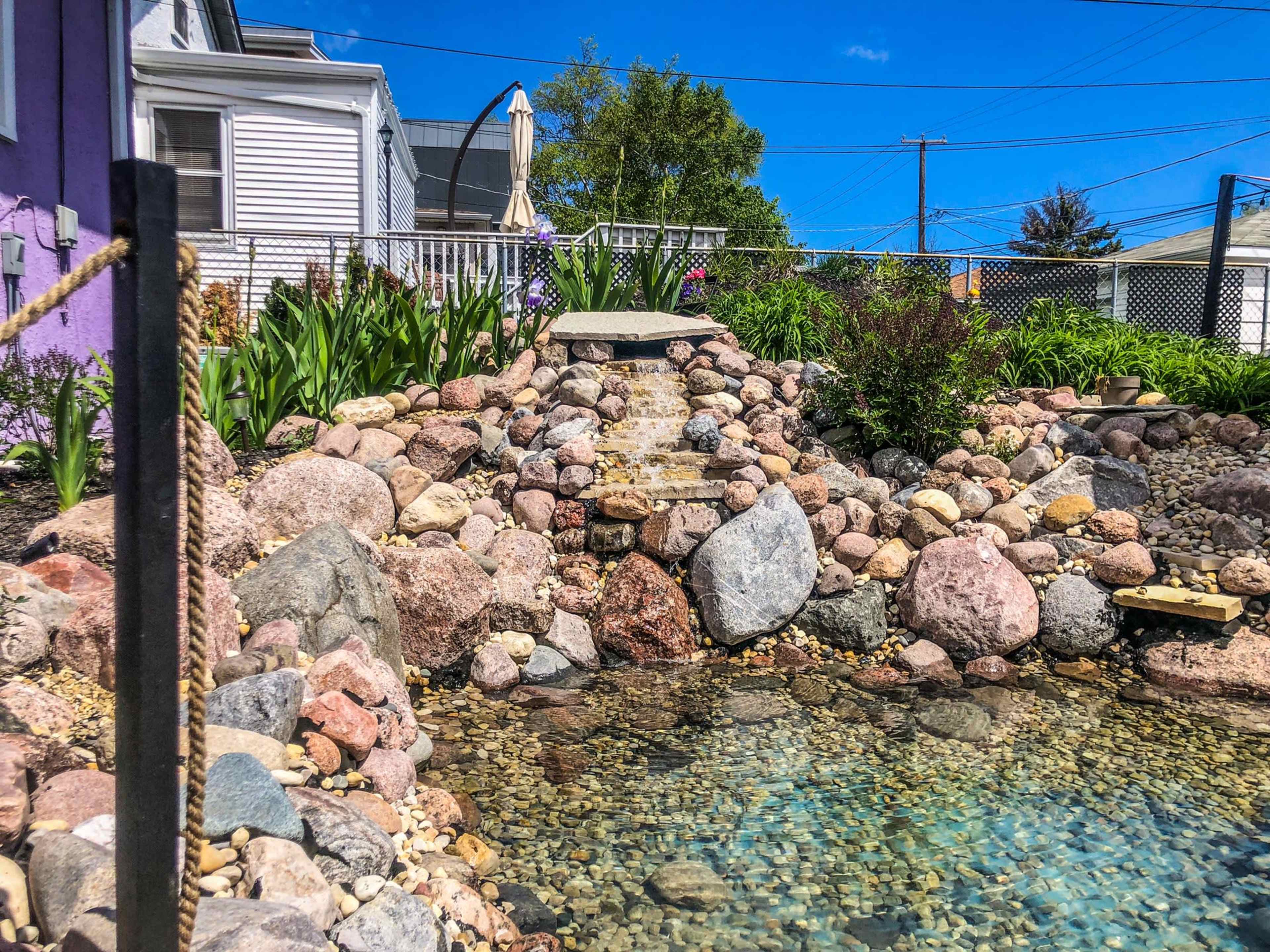 A landscaped pond surrounded by various sized rocks and a small water feature flowing down steps.