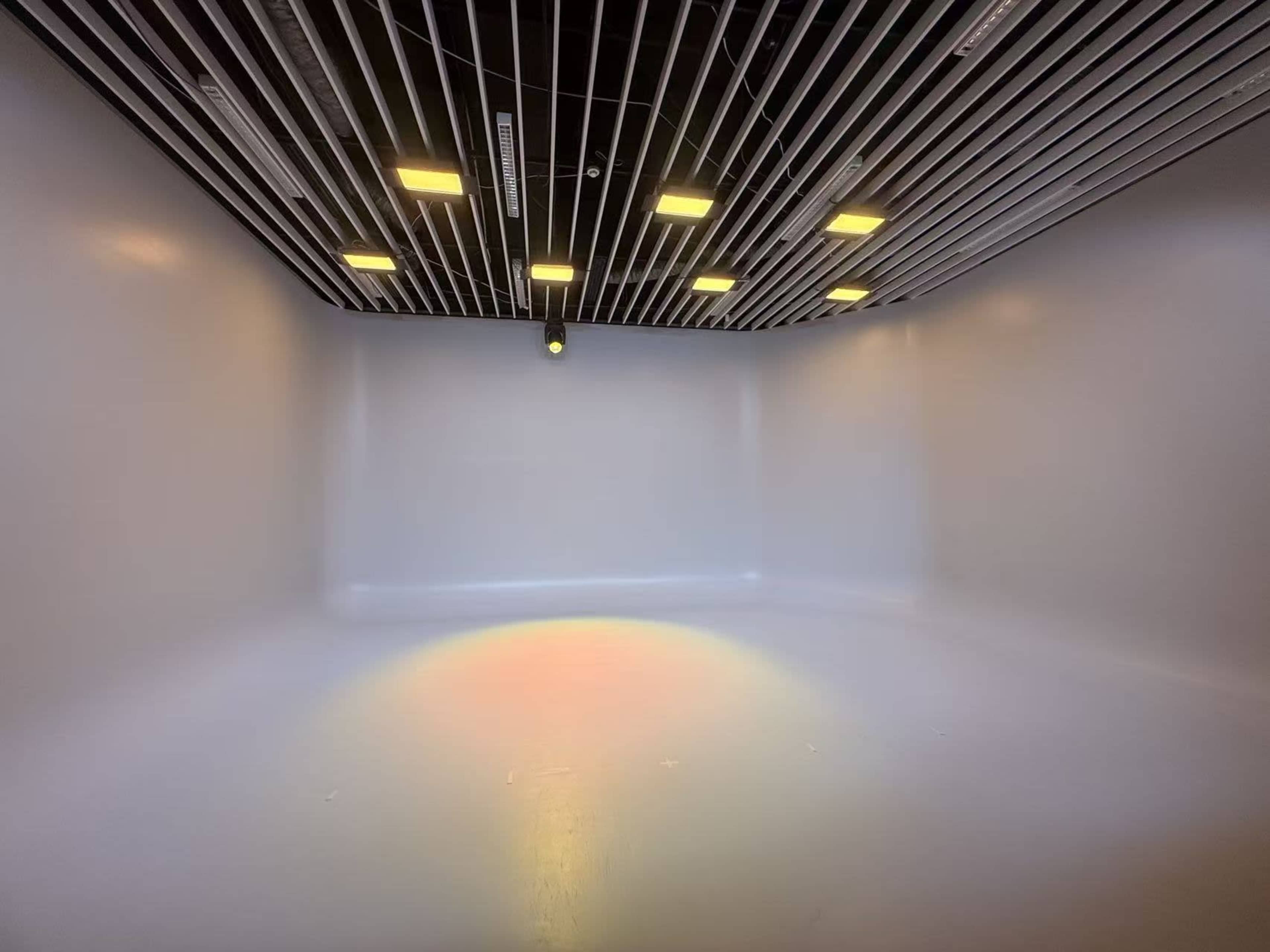 The image shows an empty room with a smooth white surface and ceiling lights arranged in a grid pattern, casting a subtle rainbow effect on the floor.