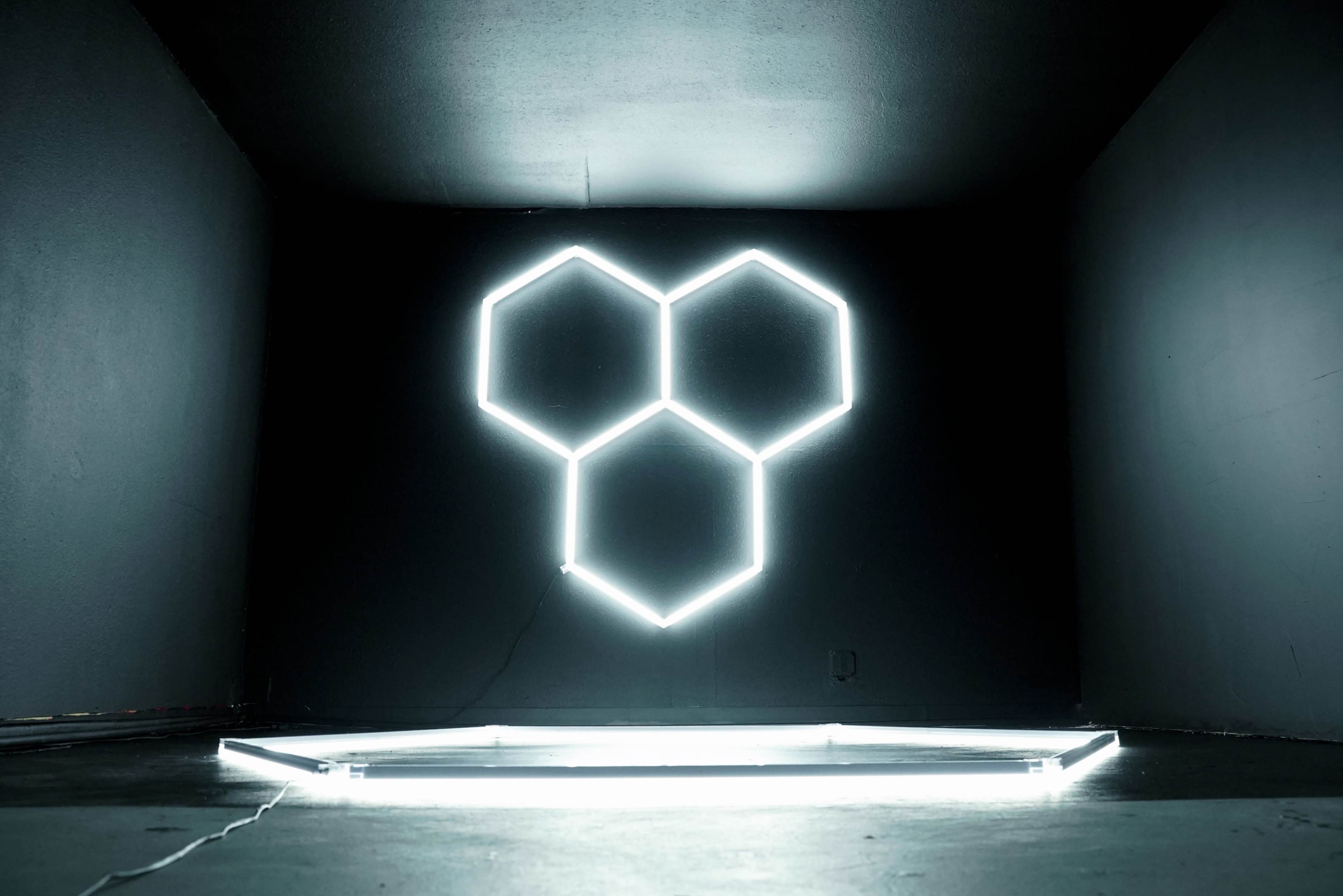 The image features a dark room with a wall displaying three interconnected hexagonal neon lights.