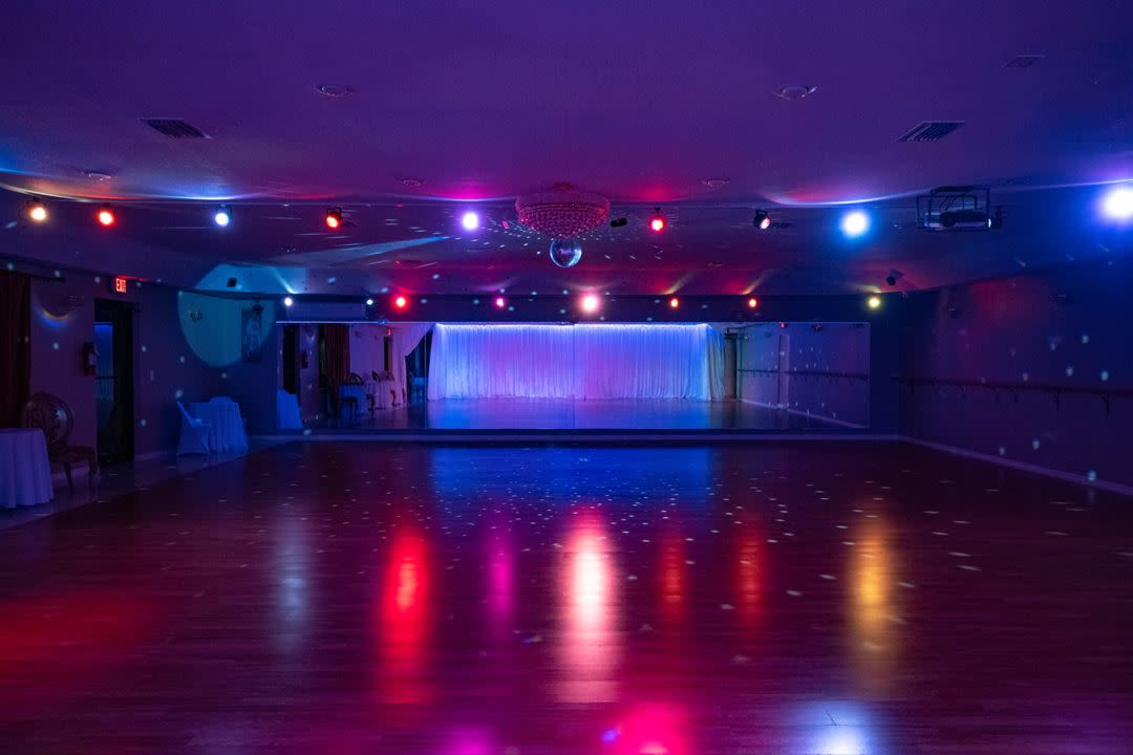 The image shows a brightly lit dance studio with colorful spotlights and reflective surfaces on the floor.