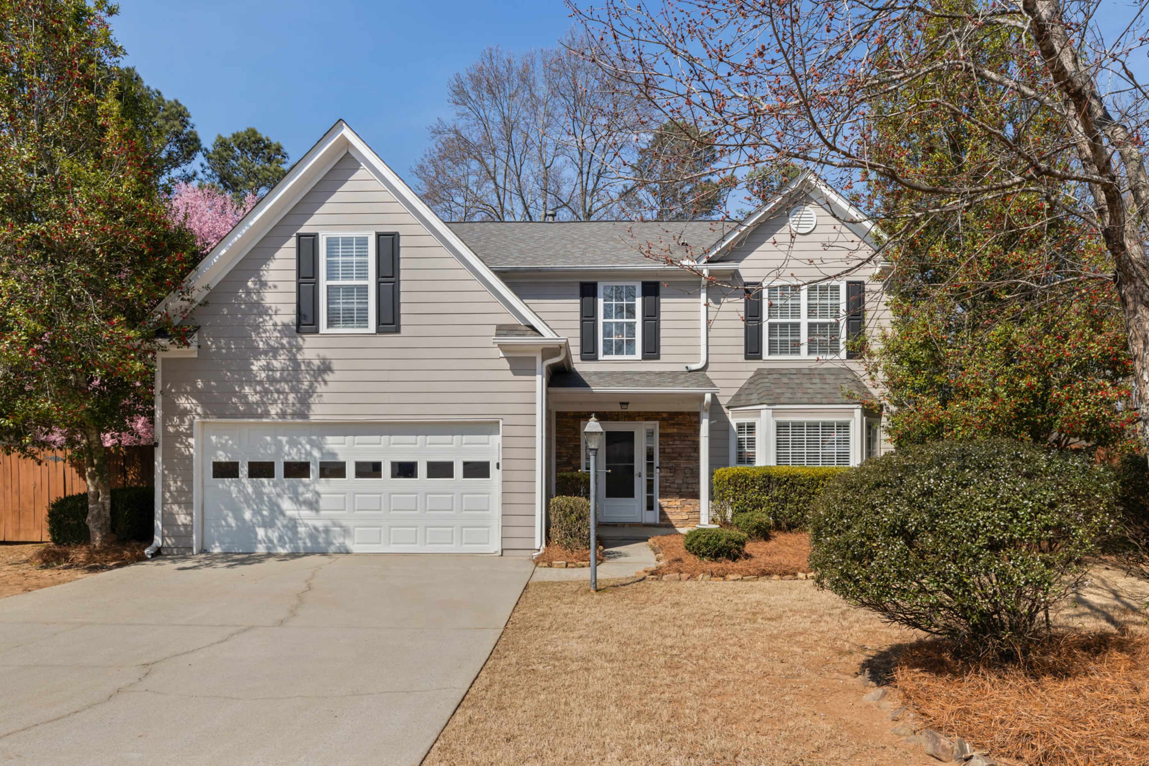 A two-story house with a light exterior, front porch, and attached garage is set in a landscaped yard.