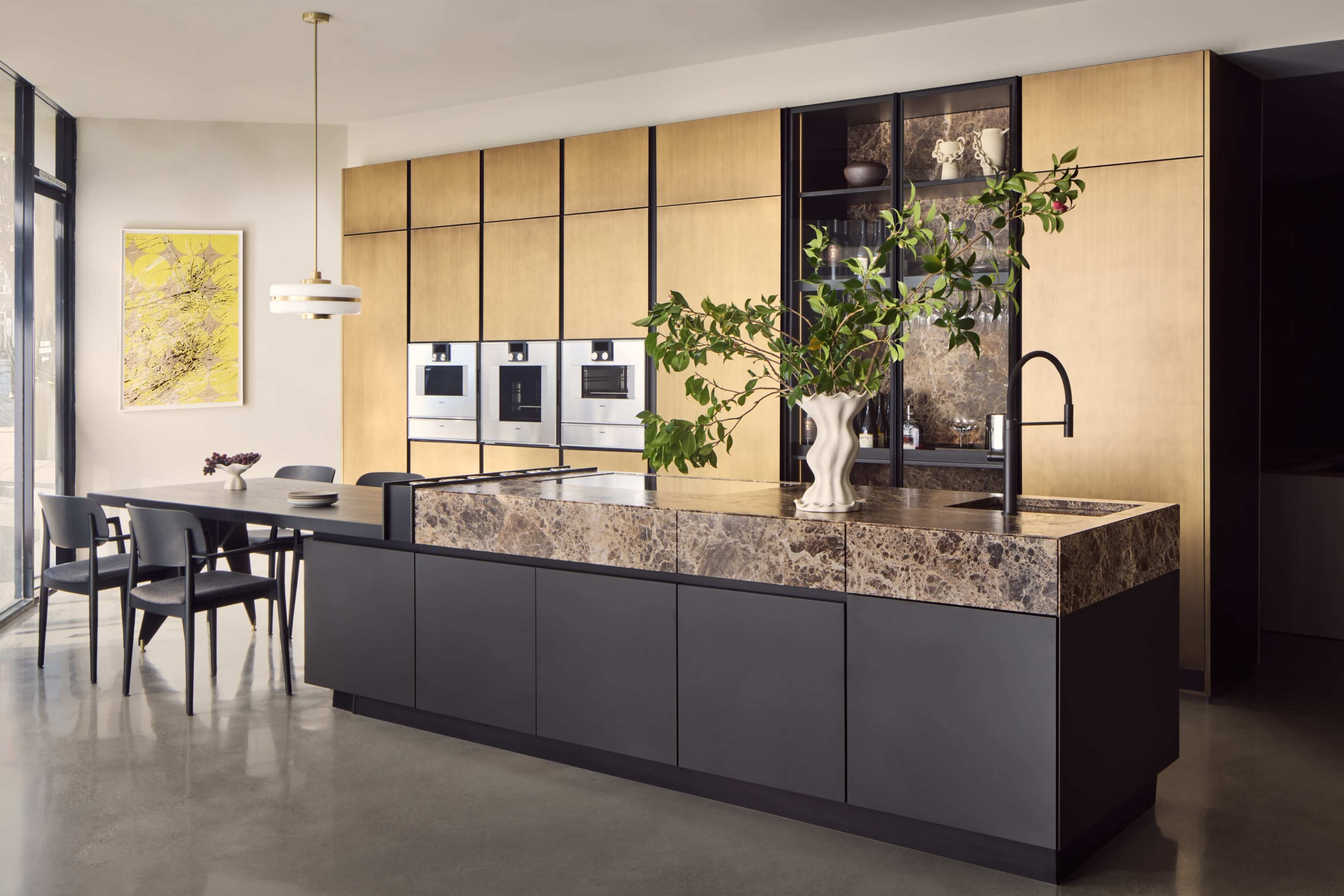 The image features a modern kitchen with a dark cabinetry base, light wood paneling, a marble countertop, and a dining area with black chairs.