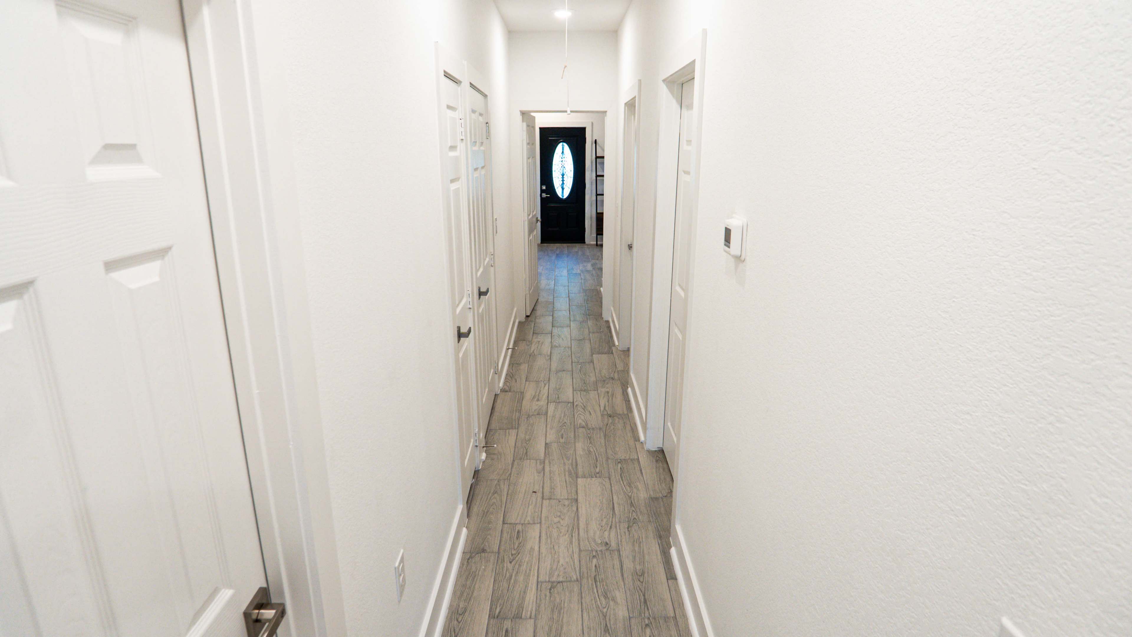 The image shows a long, narrow hallway with white walls and several doors leading to different rooms.