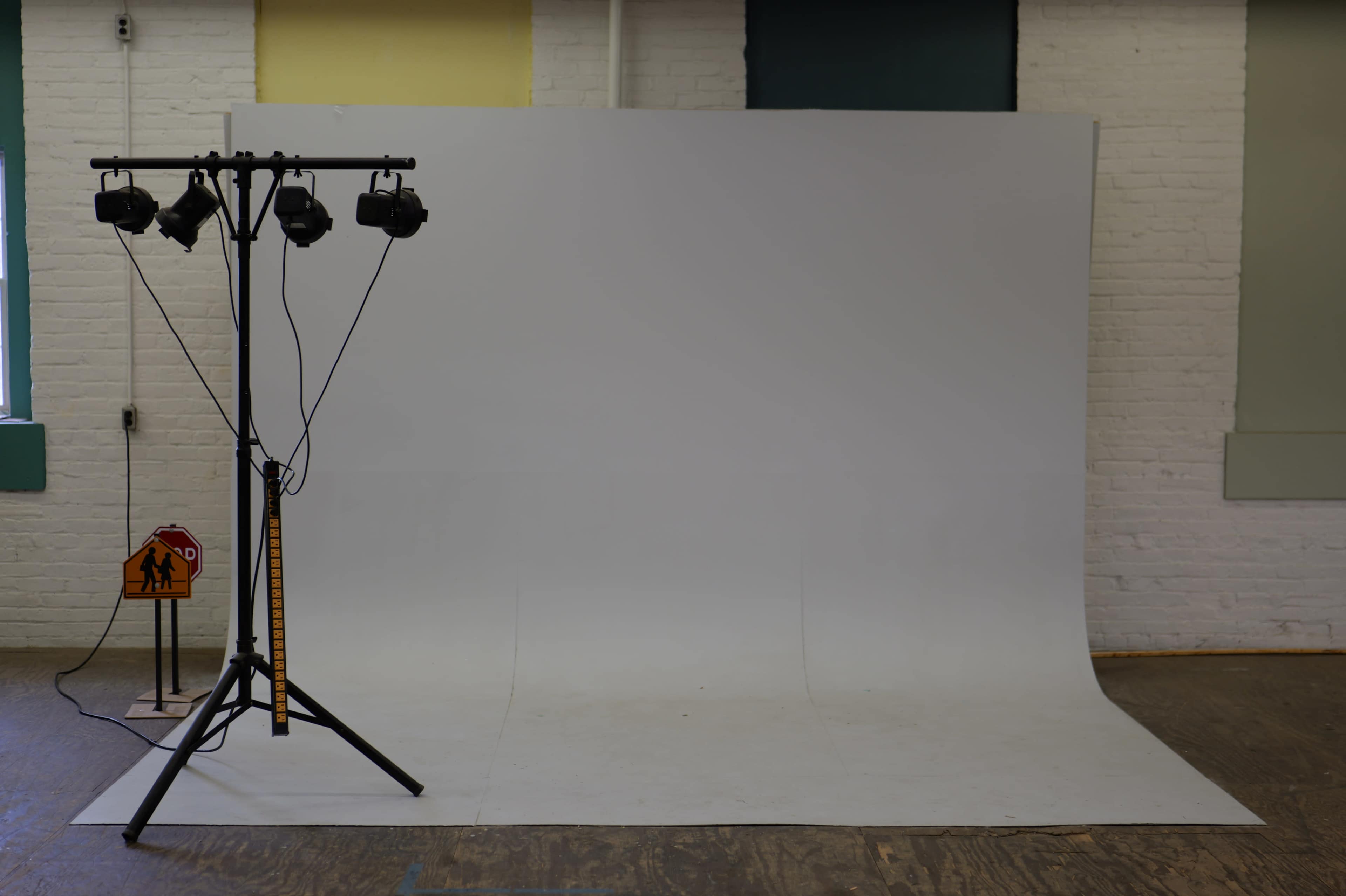 A photography studio features a white backdrop, lighting rig, and a caution sign on the floor.
