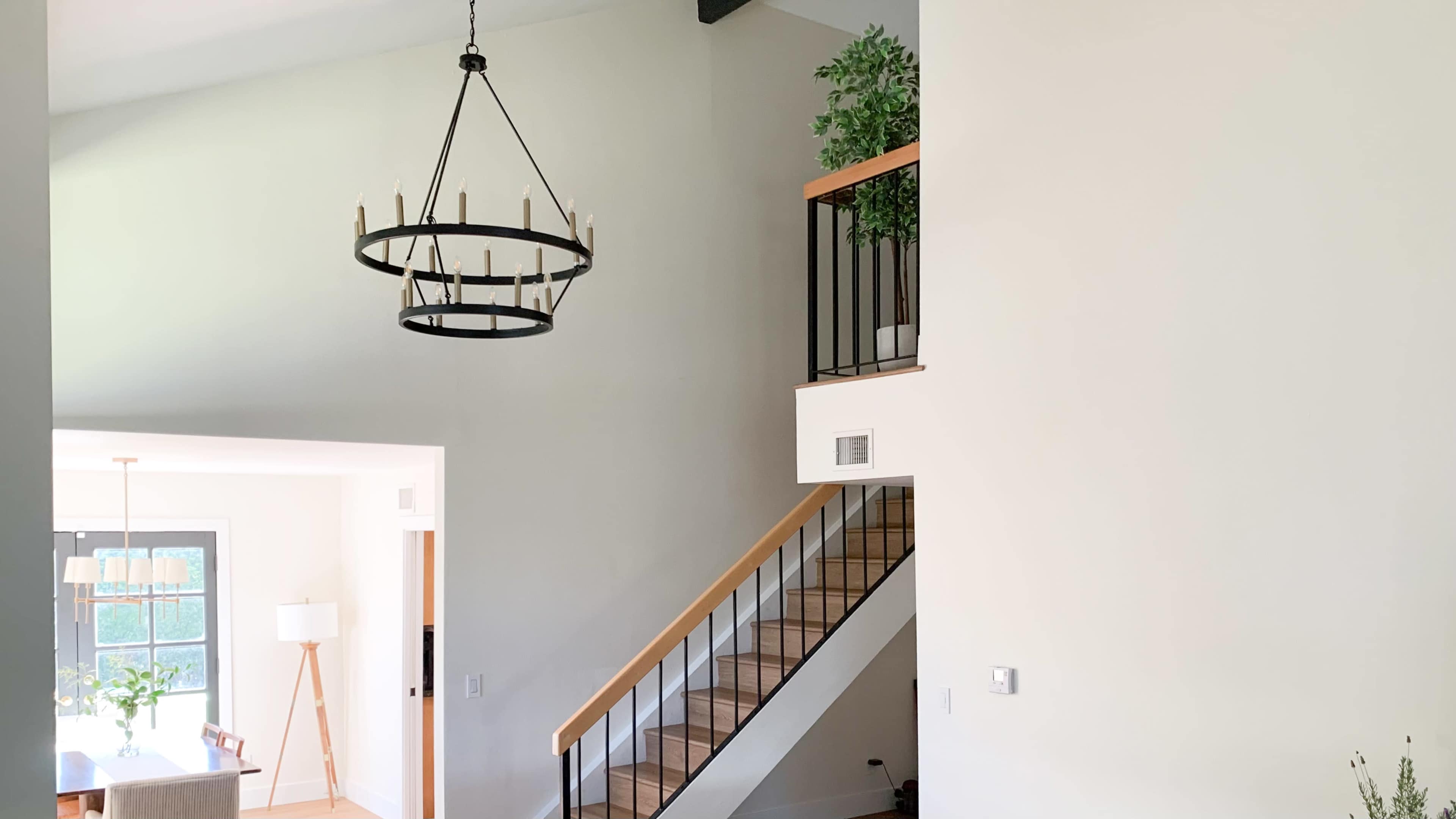 A bright interior space with a modern chandelier, a staircase leading to an upper landing, and a potted plant on the railing.