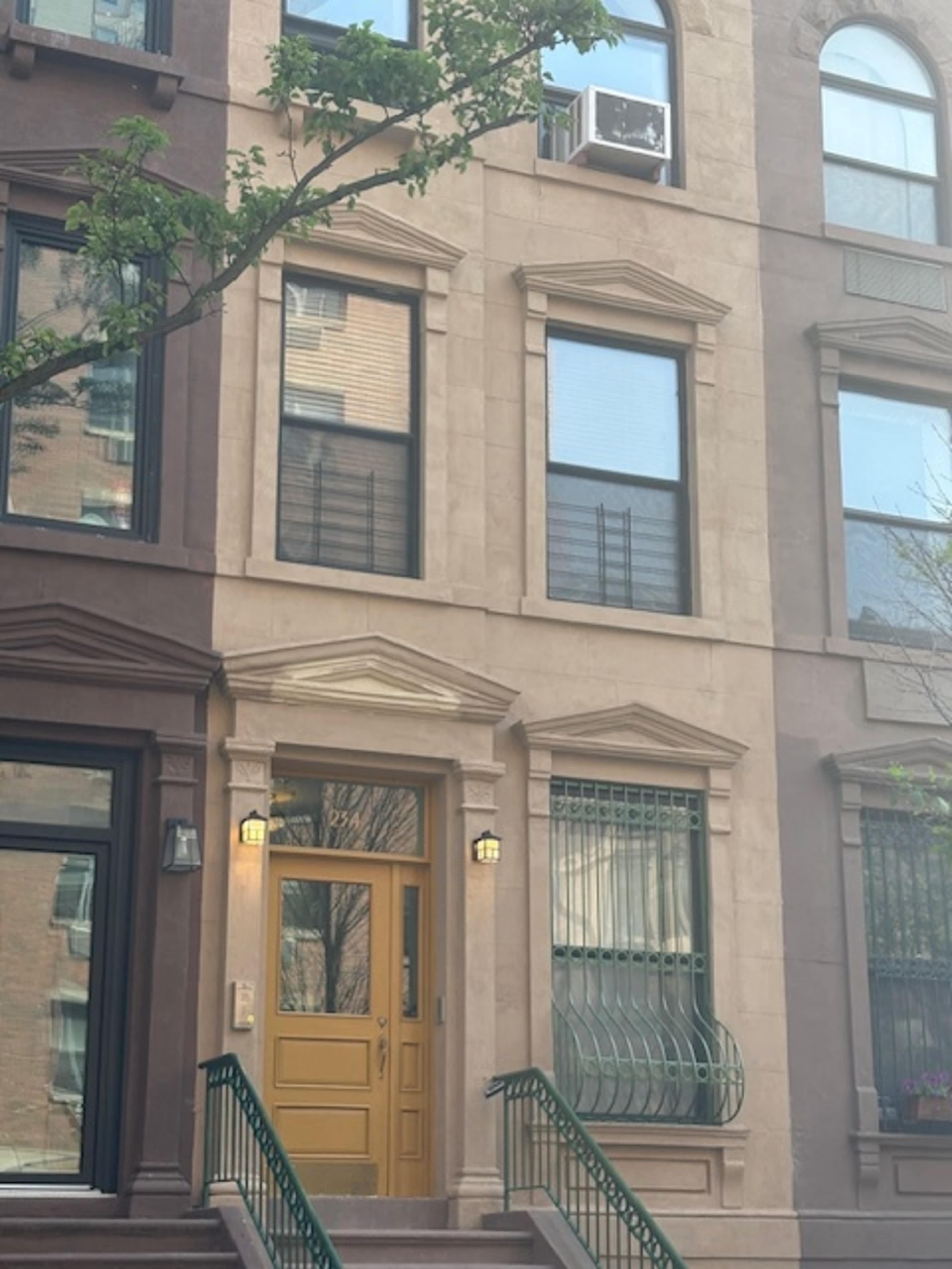 The image shows the facade of a brownstone building with a prominently featured yellow door and large windows.