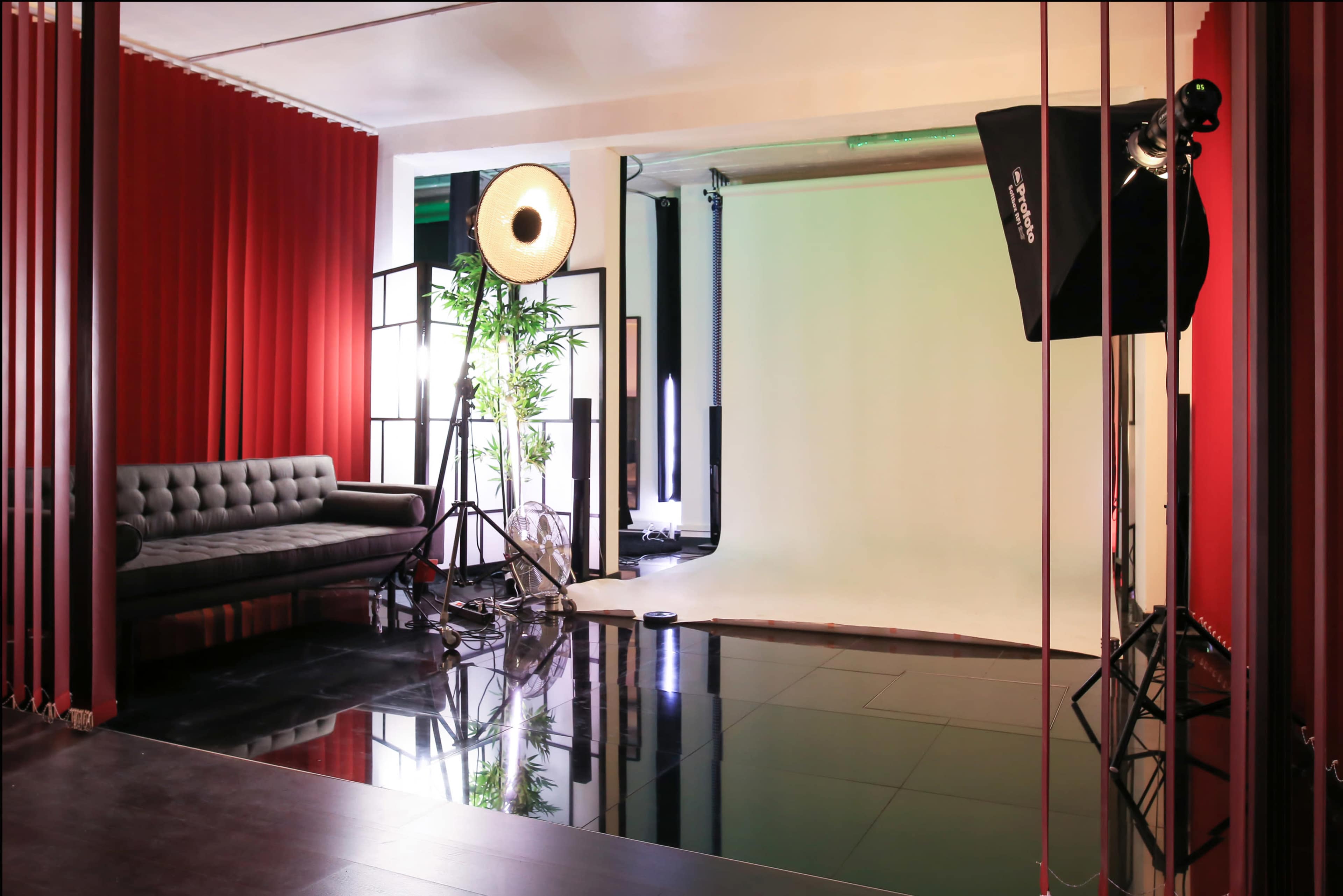 The image shows a photography studio with a black couch, a large light source on a stand, and a green backdrop.