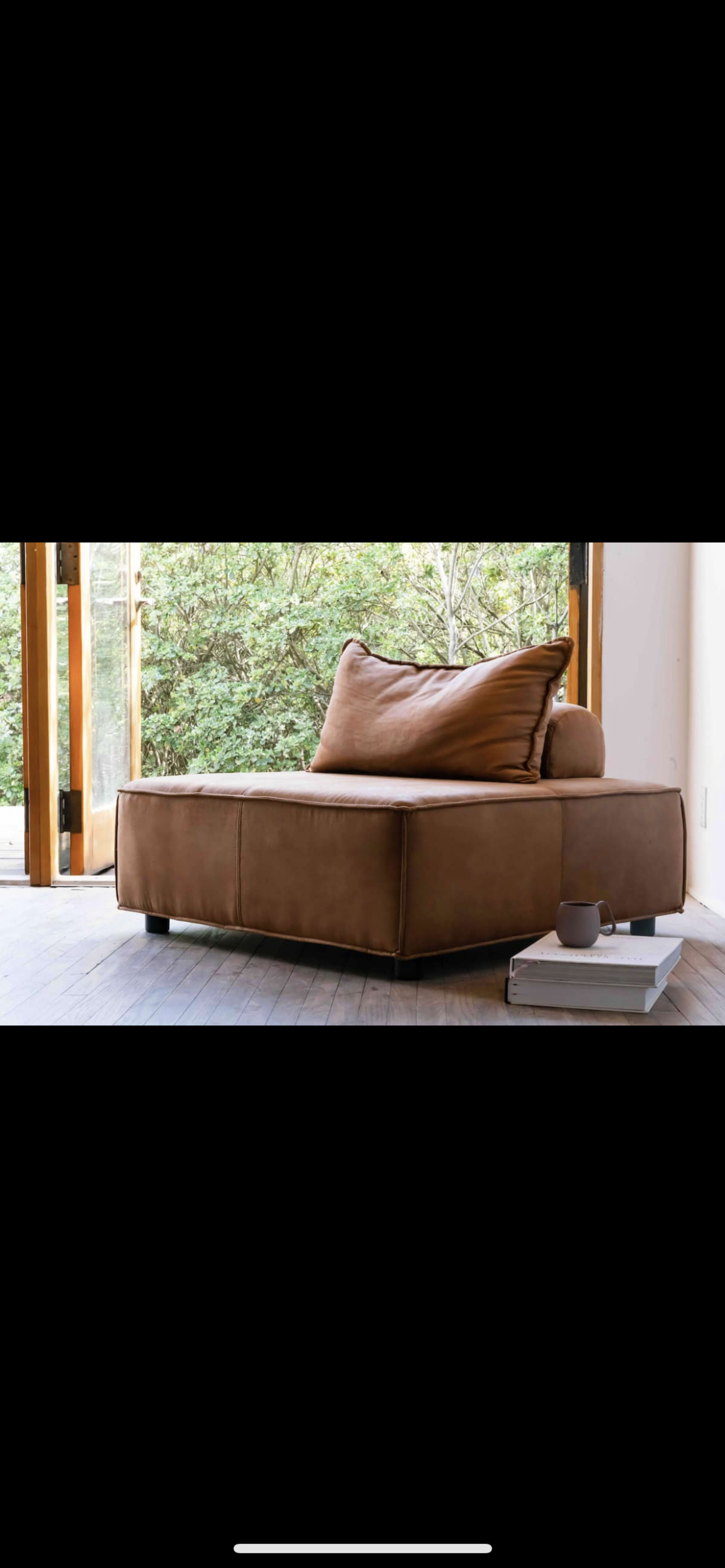A brown leather chaise lounge is positioned next to an open window, with a book resting on the floor nearby.