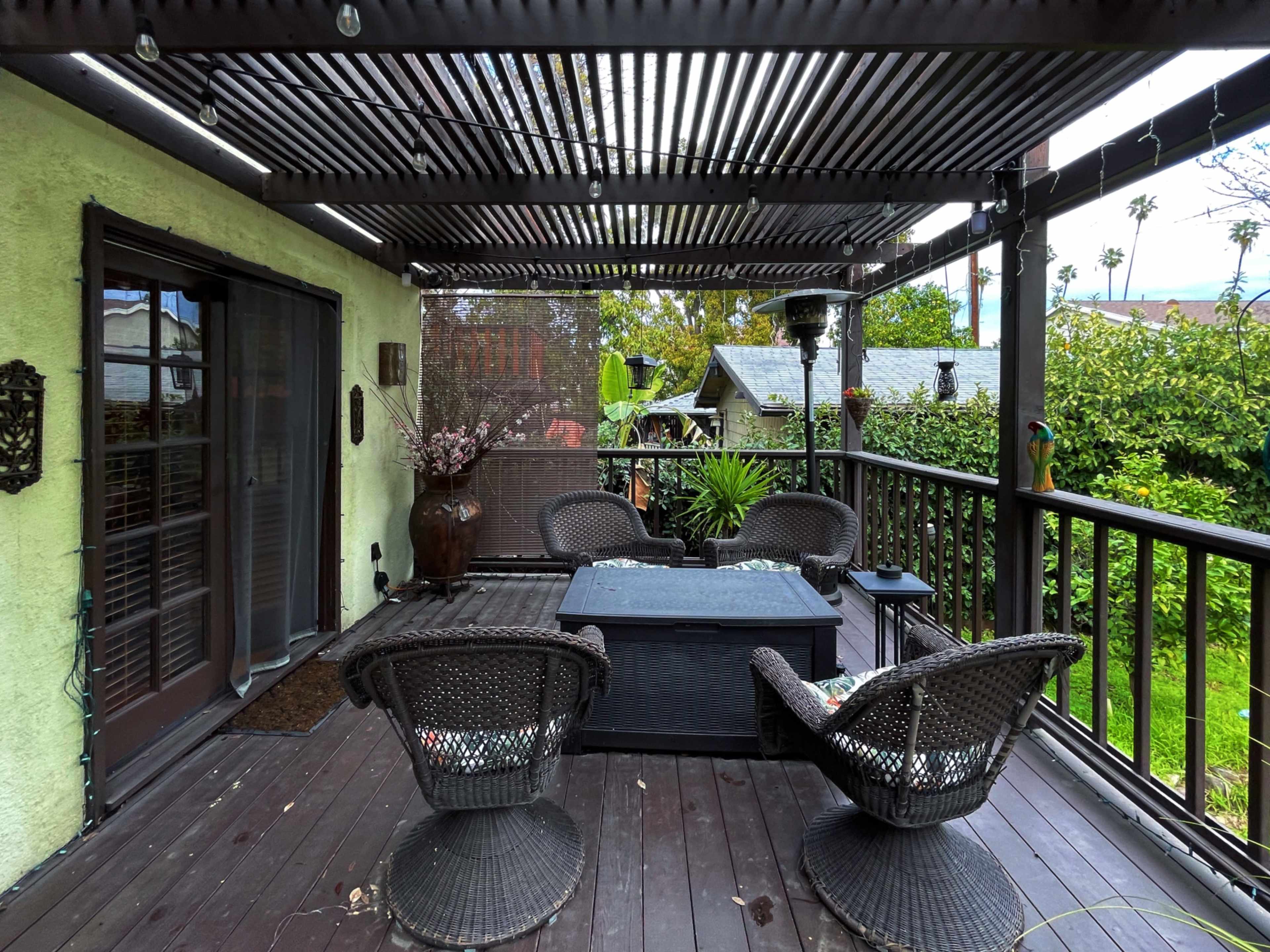 A patio with a wooden deck featuring four wicker chairs and a coffee table under a slatted pergola.