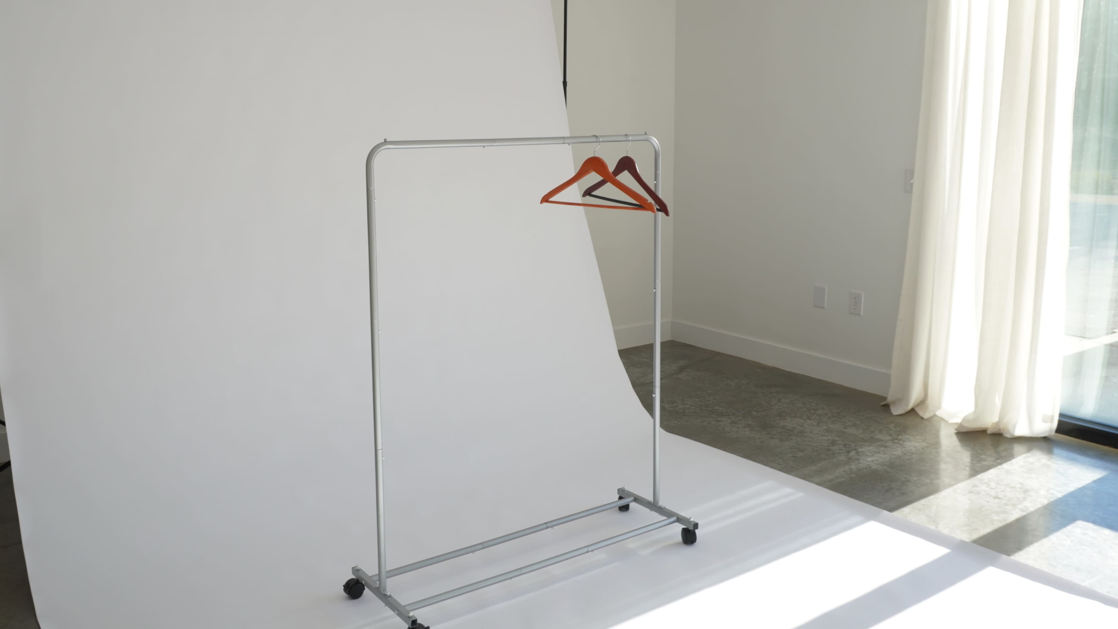 A clothing rack with three wooden hangers is positioned against a plain white backdrop in a well-lit room.