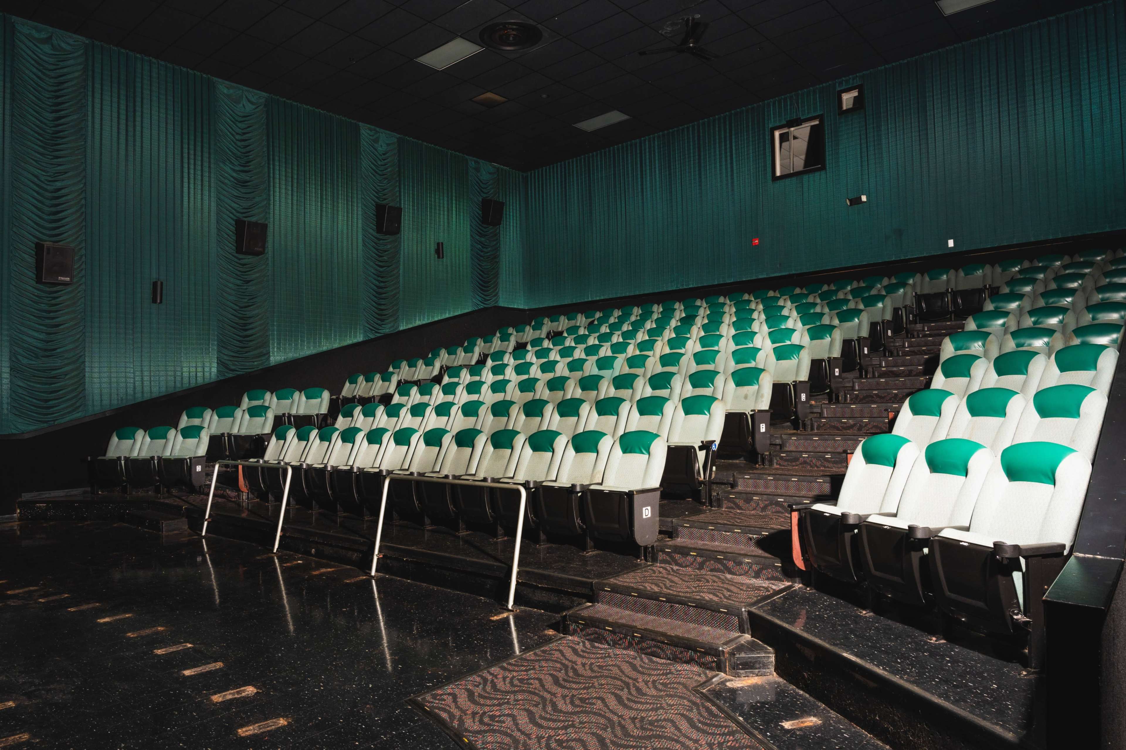 A movie theater with empty green and white seats arranged in rows on a dark carpeted floor.