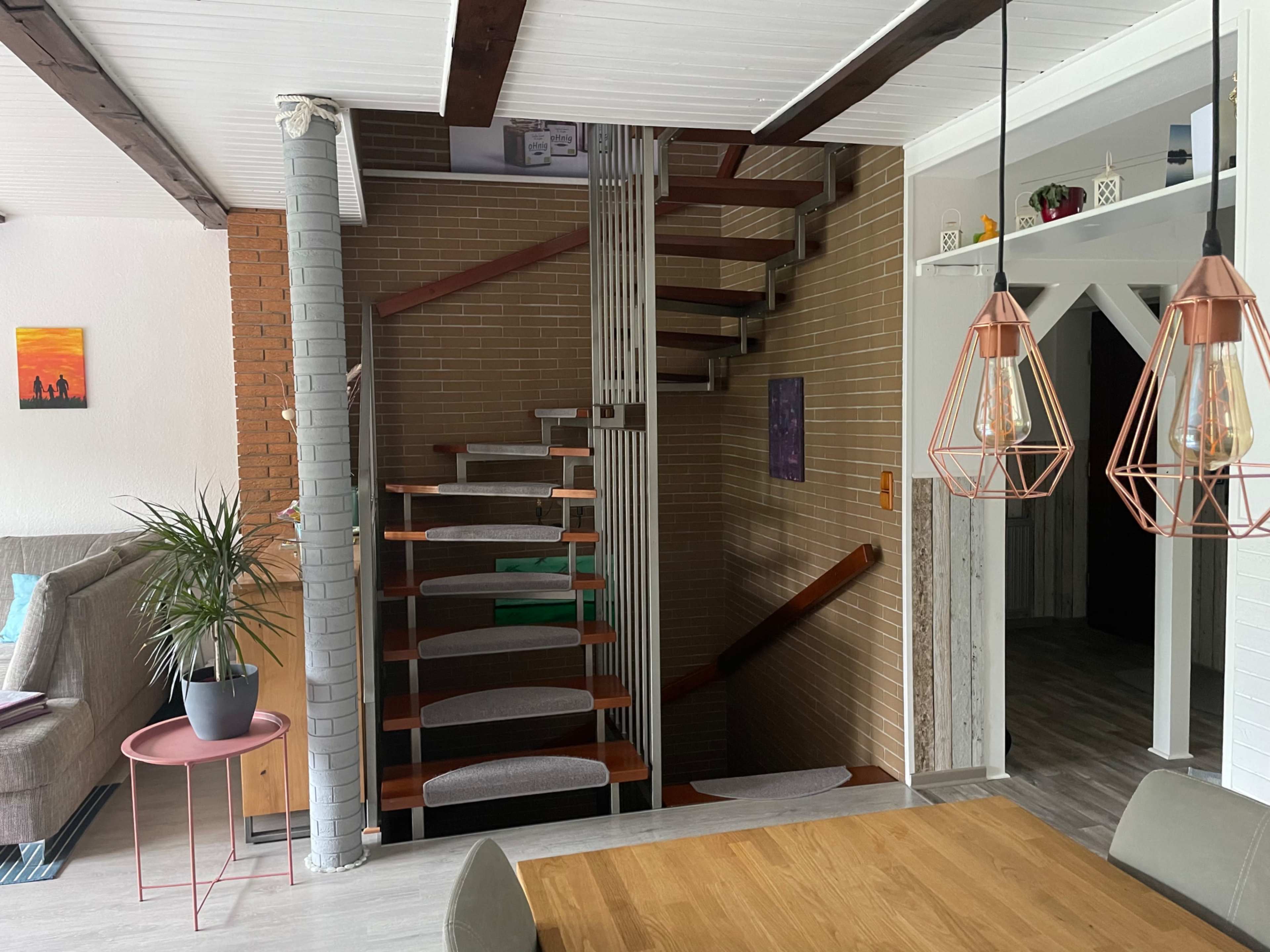 A wooden staircase leads from a living area to an upper level, with a dining table and pendant lights visible in the foreground.