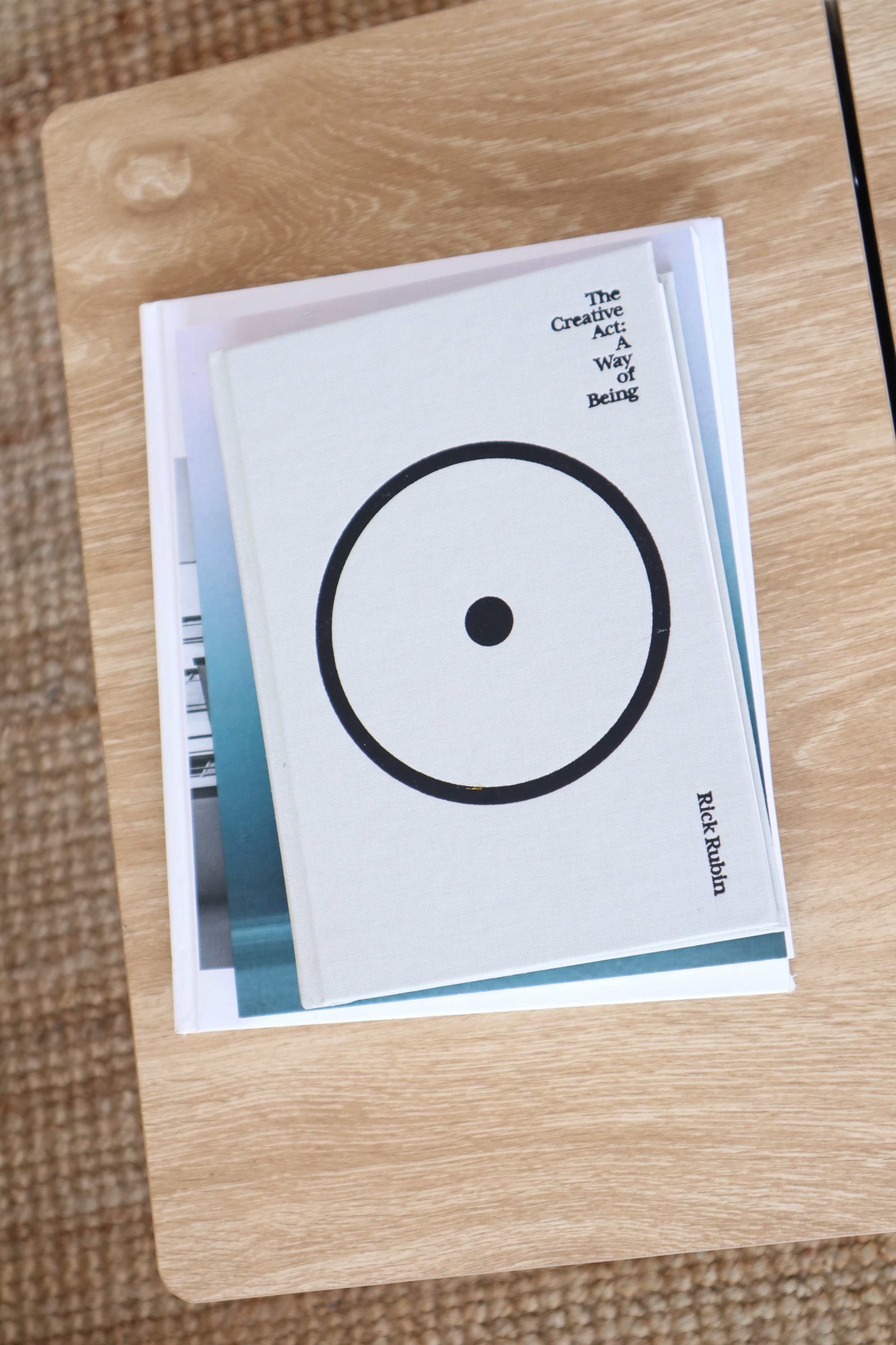 A book with a plain cover featuring a large circle is placed on a wooden table alongside other papers.
