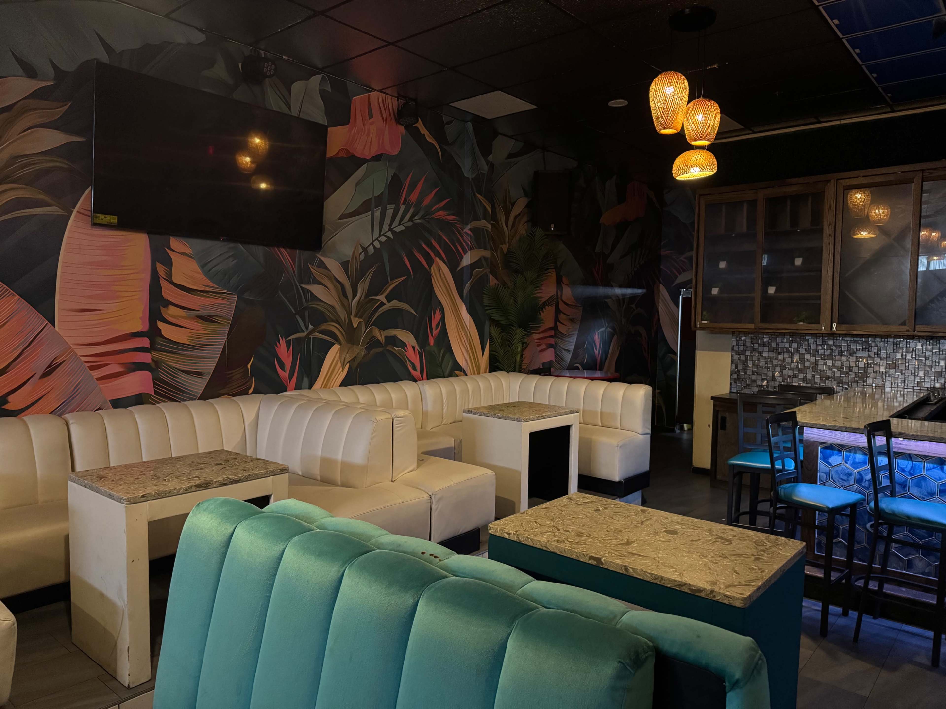 The image shows a modern lounge area with white and teal seating, marble-topped tables, and a tropical-themed mural on the walls.
