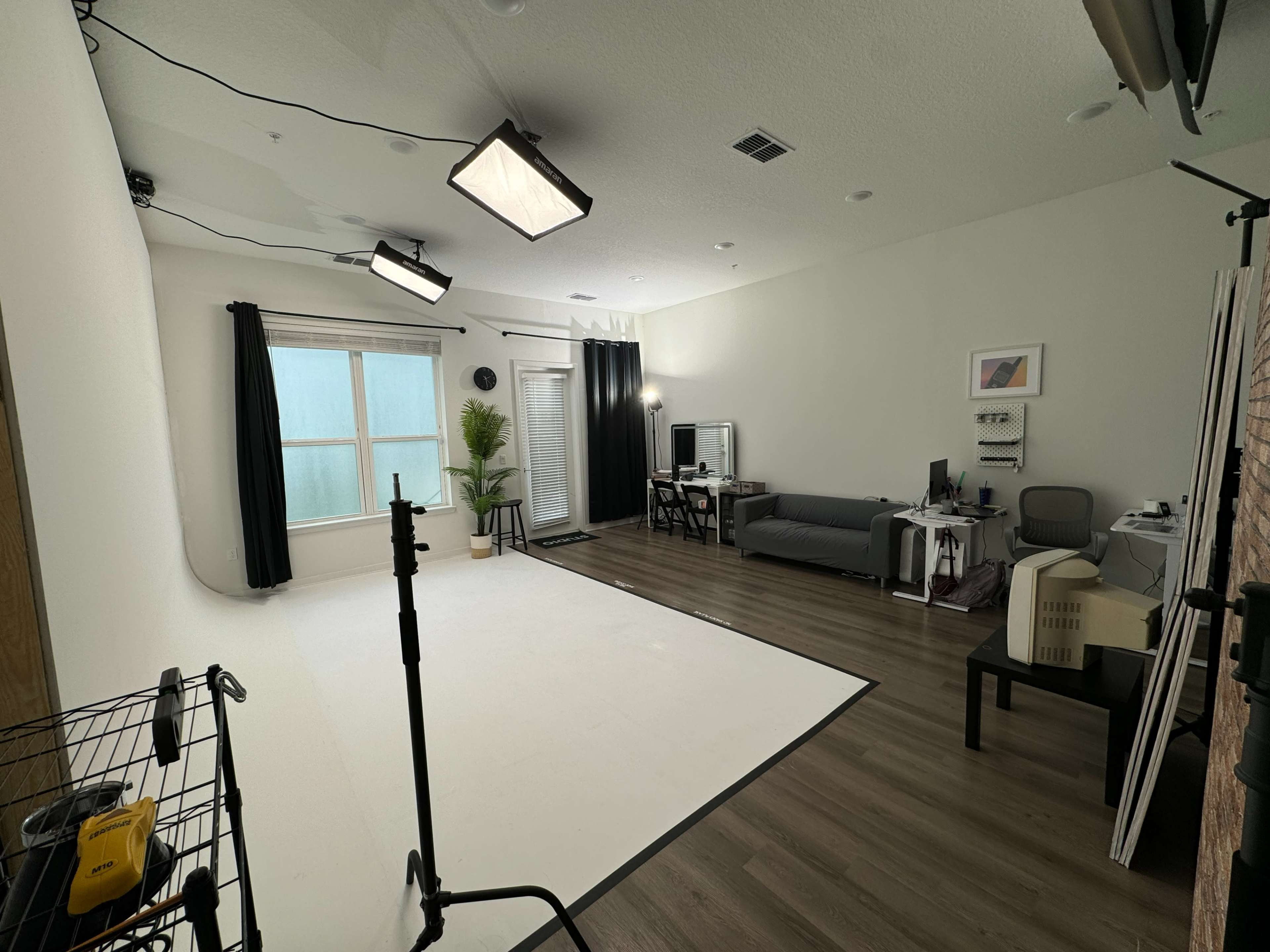 The image shows a spacious studio space with a white backdrop, a couch, a desk with a computer, and studio lighting equipment.