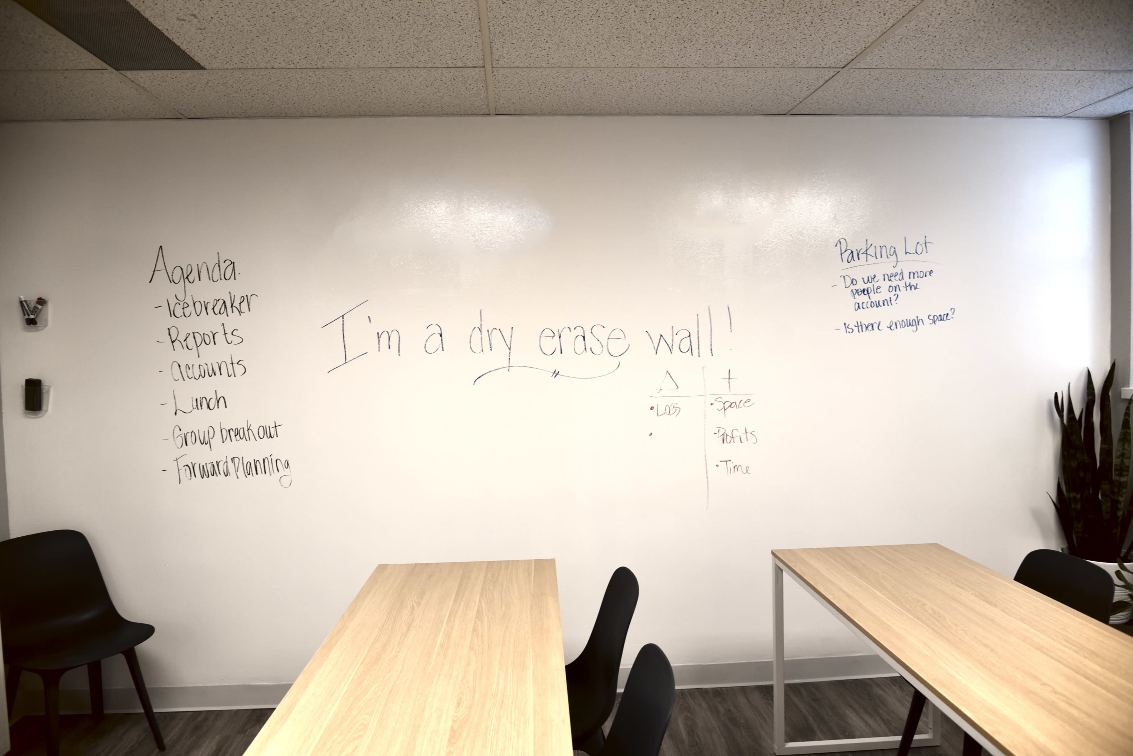 A white dry erase wall in a meeting room with an agenda list and a handwritten message stating, "I'm a dry erase wall!" along with a calendar and parking lot notes.
