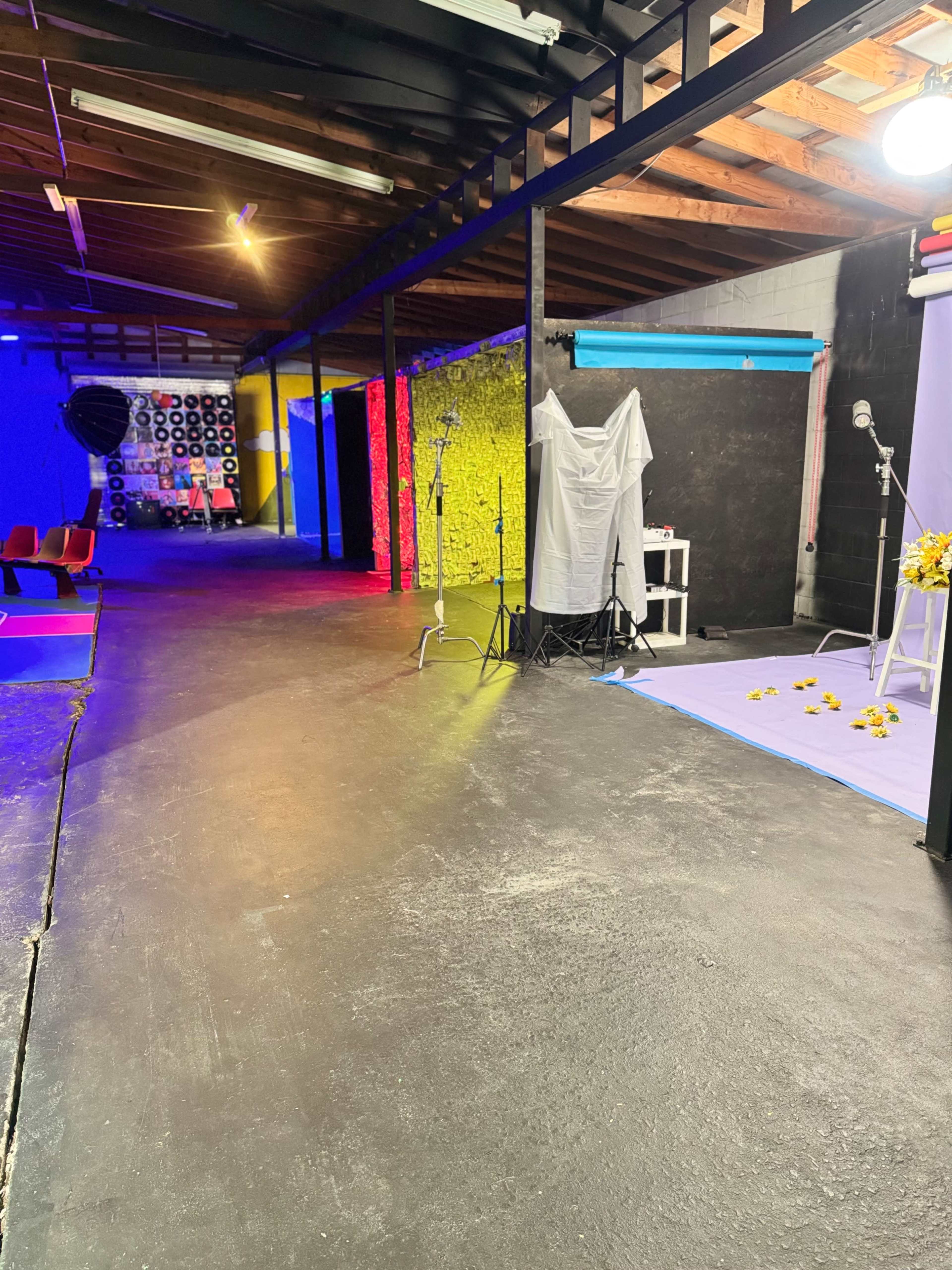 The image shows a spacious studio with colorful walls and various equipment, including lights and backdrops, set up for a photoshoot.