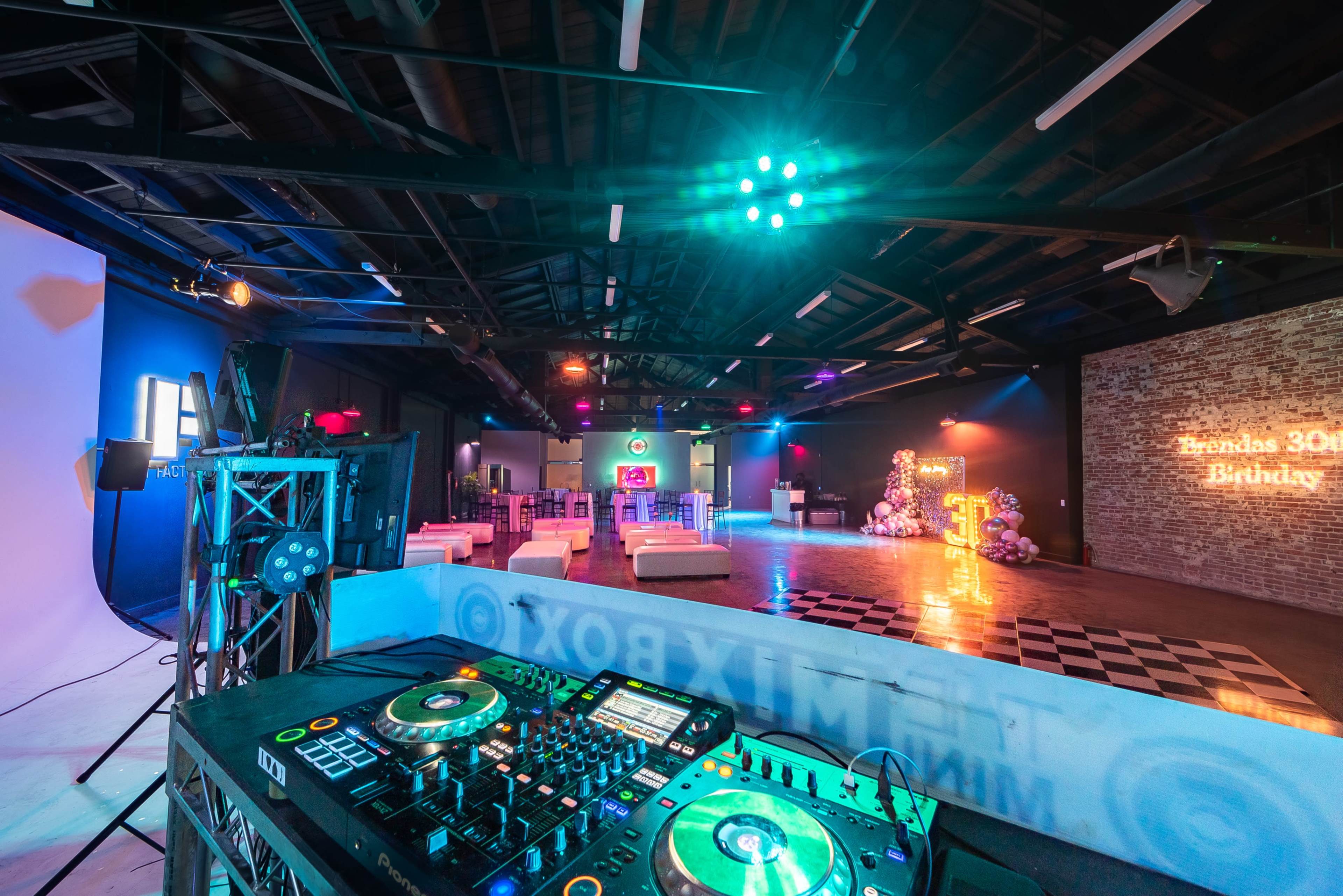 The image shows a vibrant event space set up for a birthday party, featuring a DJ setup, colorful lighting, and a dance floor.