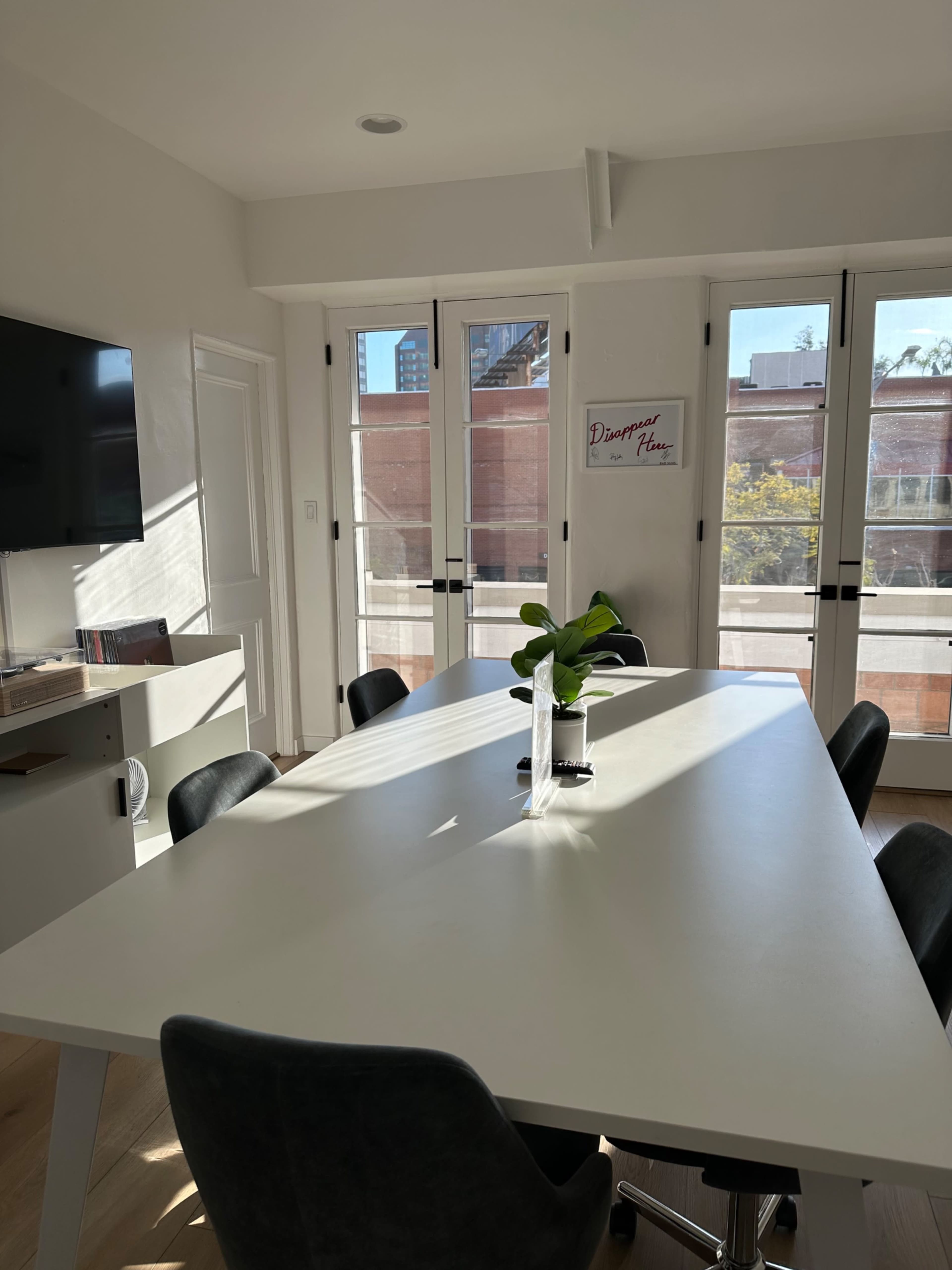 A bright conference room features a large white table surrounded by black chairs, with windows allowing natural light to illuminate the space.