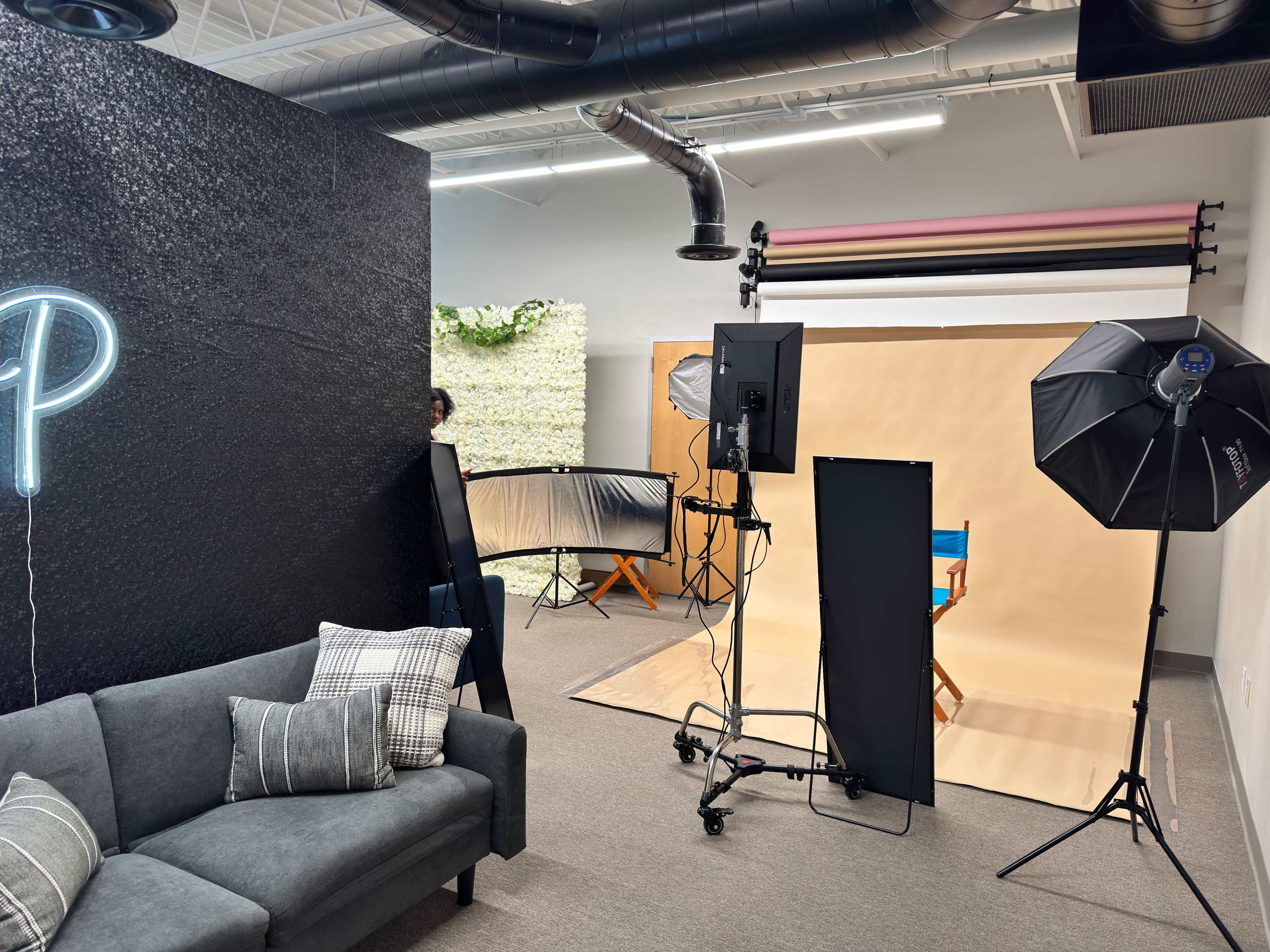 The image shows a photography studio featuring various backdrops, lighting equipment, and a gray sofa.