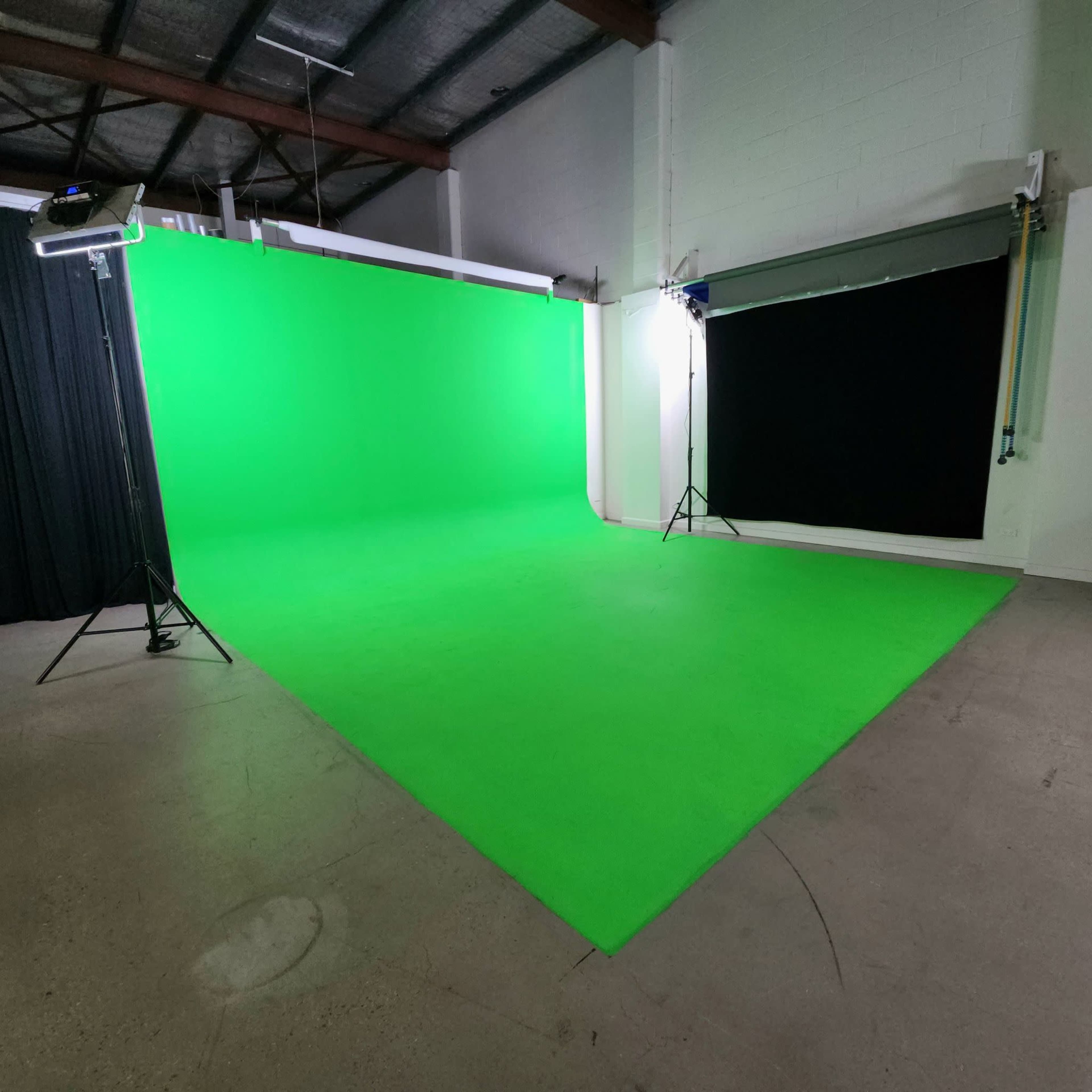 The image shows a studio space featuring a green screen backdrop with lighting equipment set up.