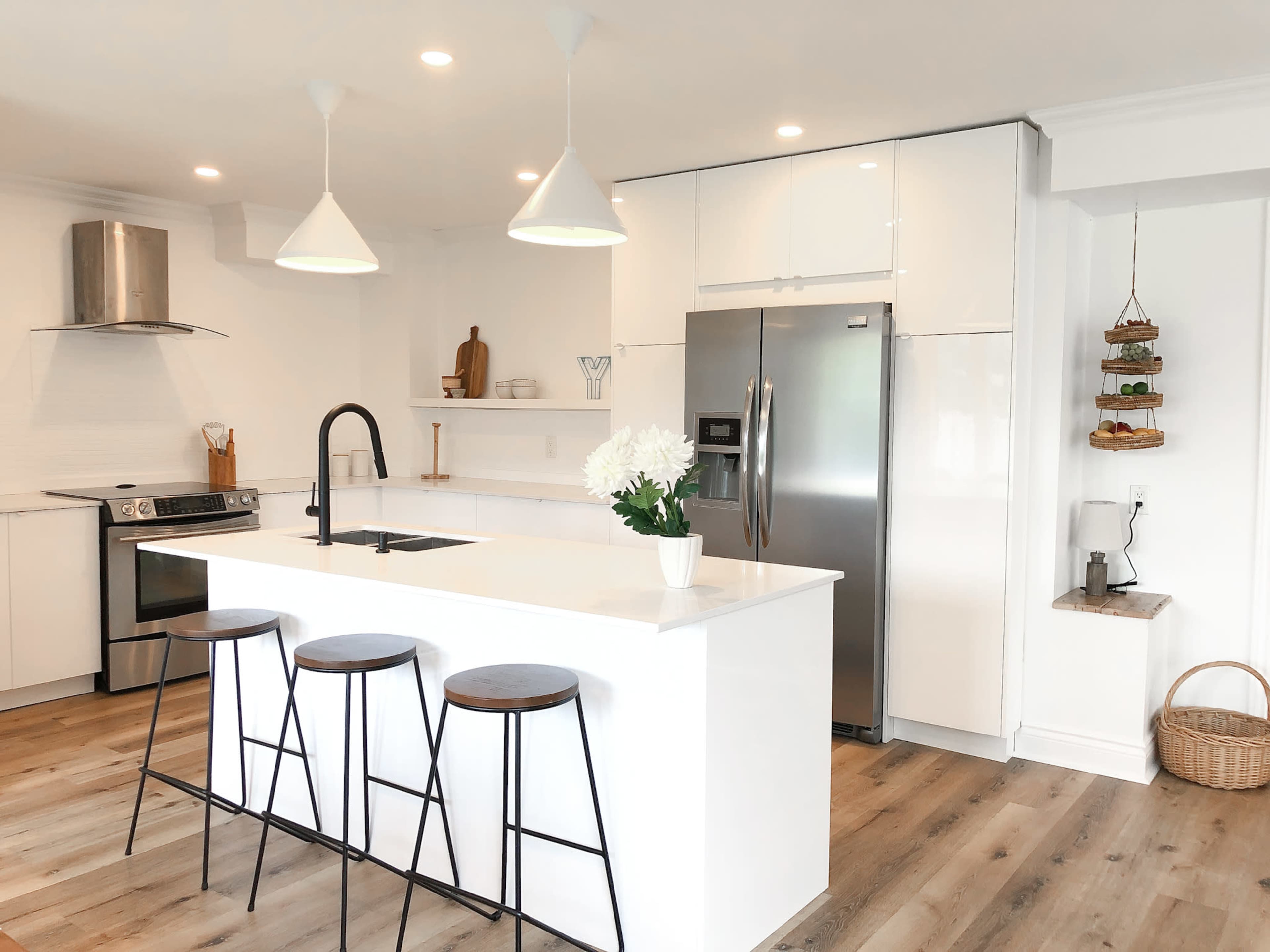 A modern kitchen features a central island with three black stools, stainless steel appliances, and white cabinetry.