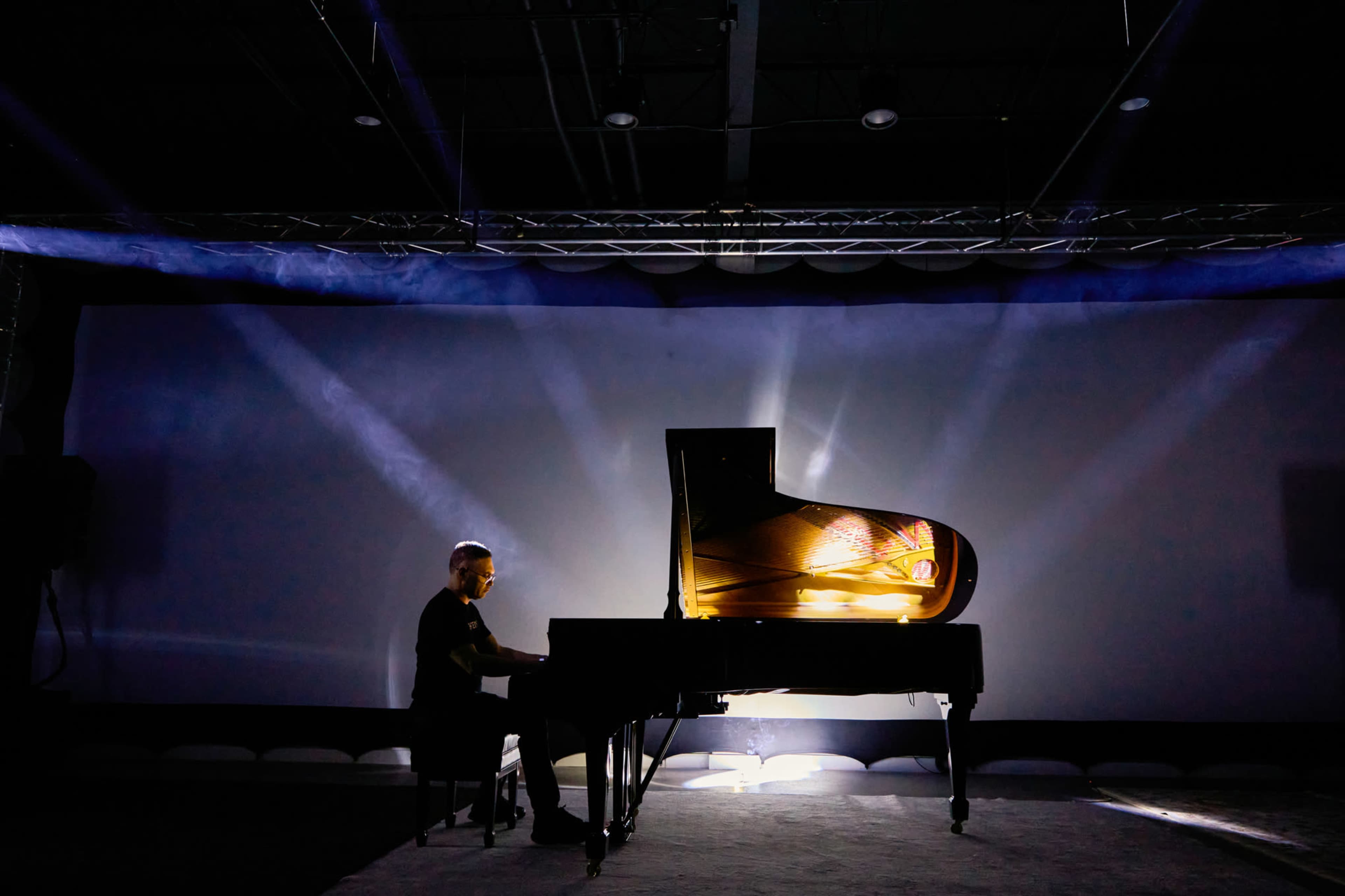 A pianist plays a grand piano illuminated by dramatic lighting in a dimly lit room.