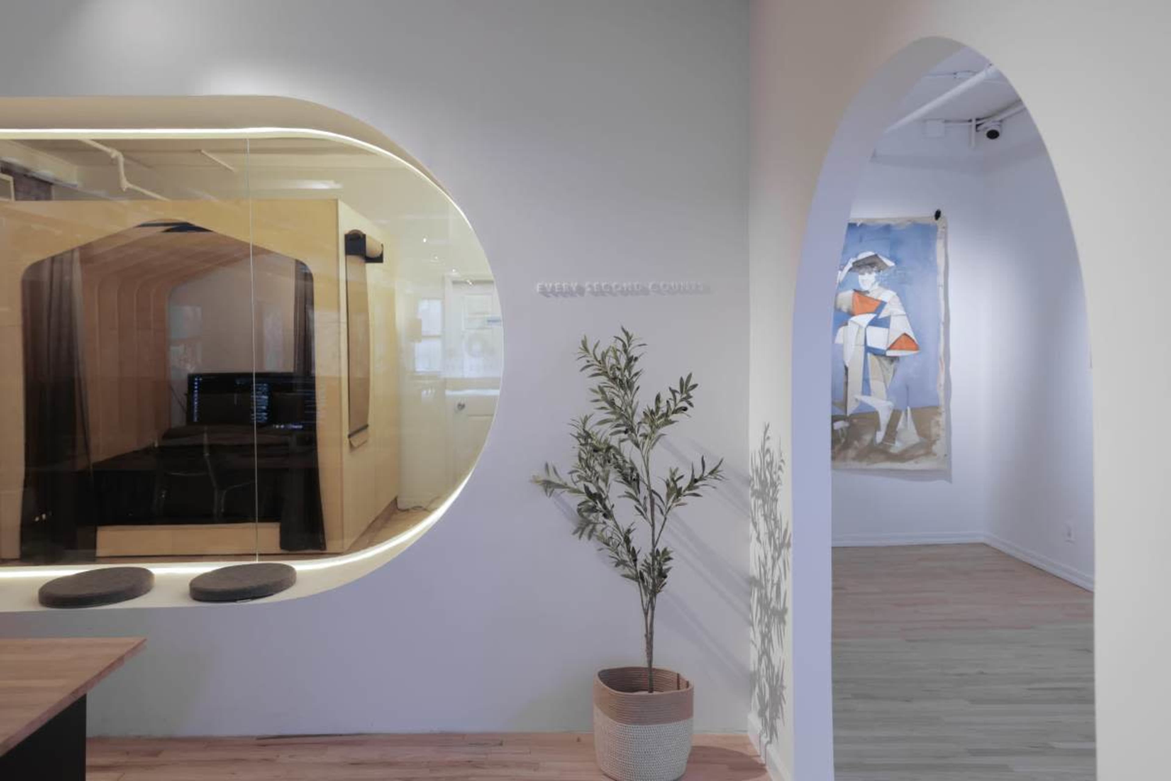The image shows a modern interior space featuring an arched entryway leading to a room with artwork, and a glass-enclosed area that appears to be a workspace or meeting room.