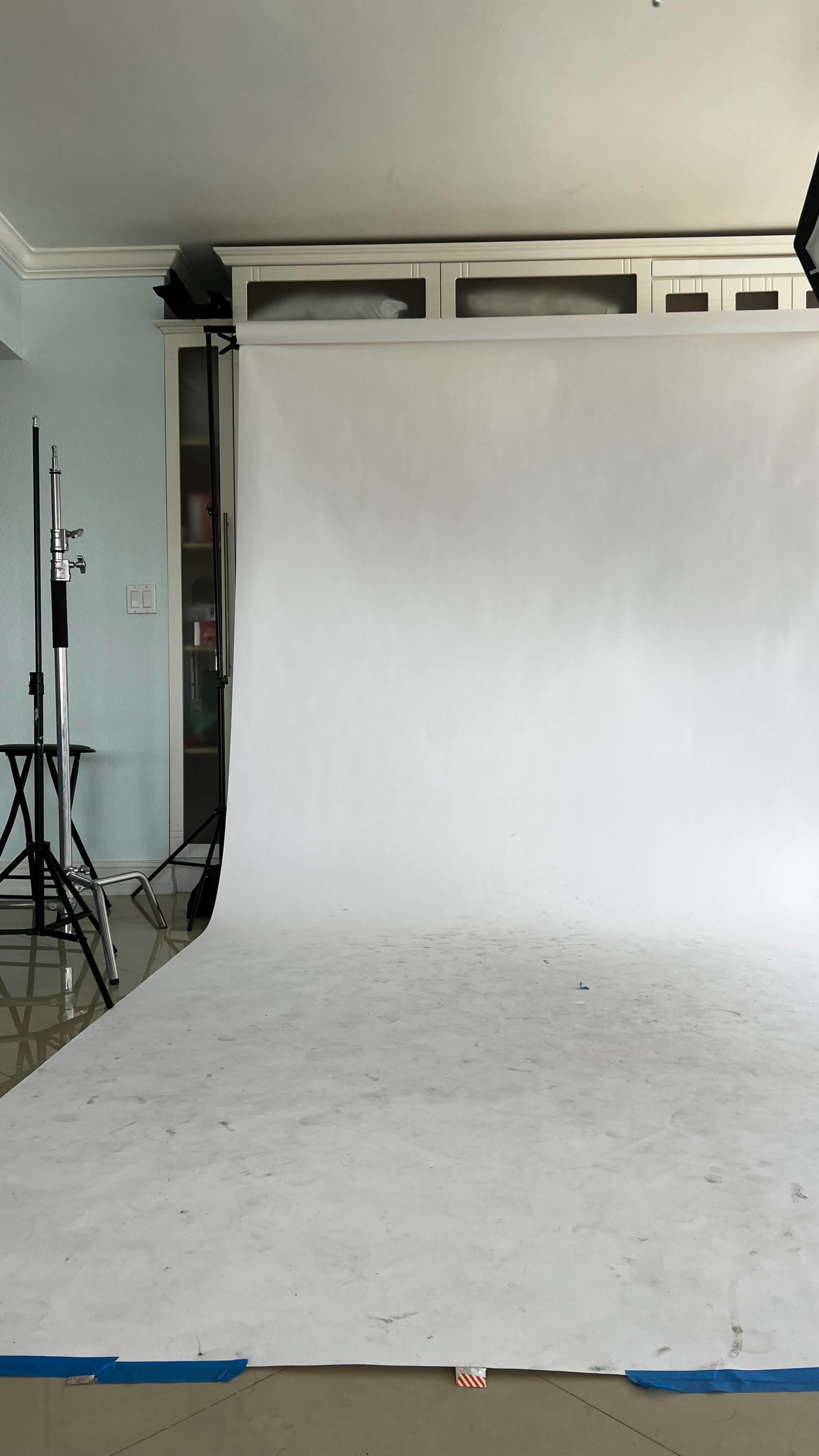 A photography studio with a white backdrop, lighting equipment, and a clean floor.