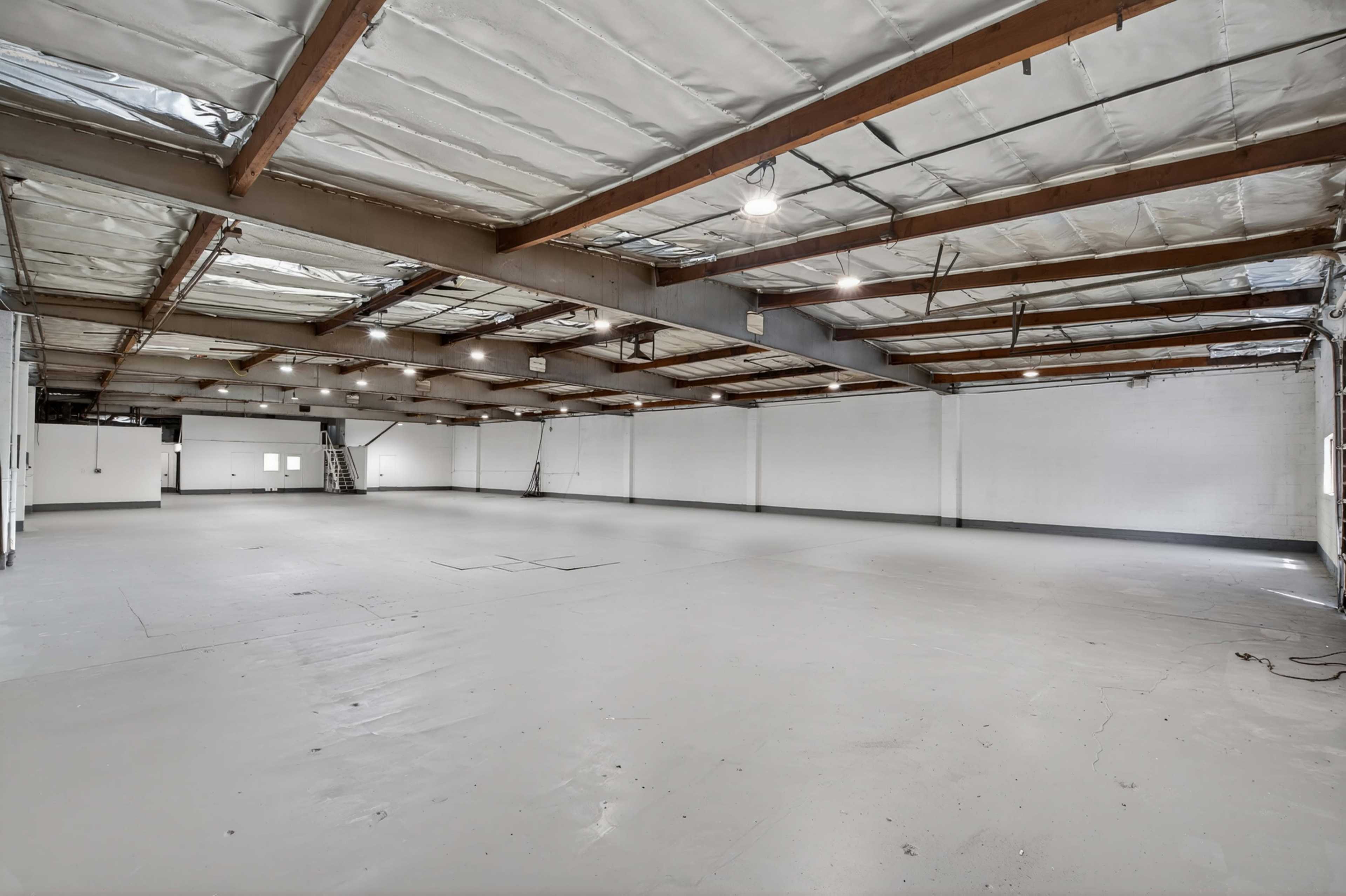 The image shows a large, empty warehouse space with exposed beams and a concrete floor.