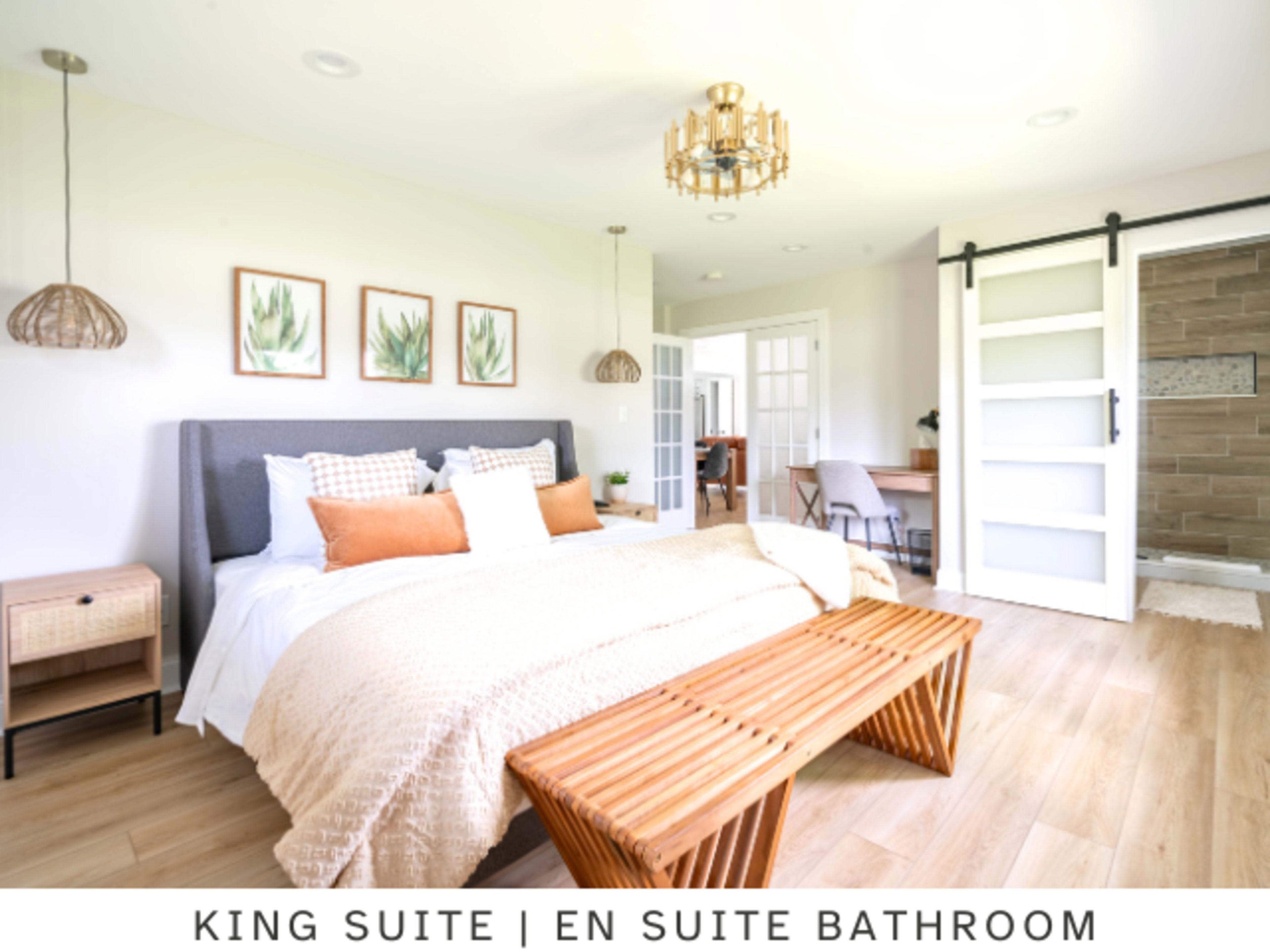 A king suite features a bed with decorative pillows, a wooden bench at the foot, and an en suite bathroom visible through a sliding door.