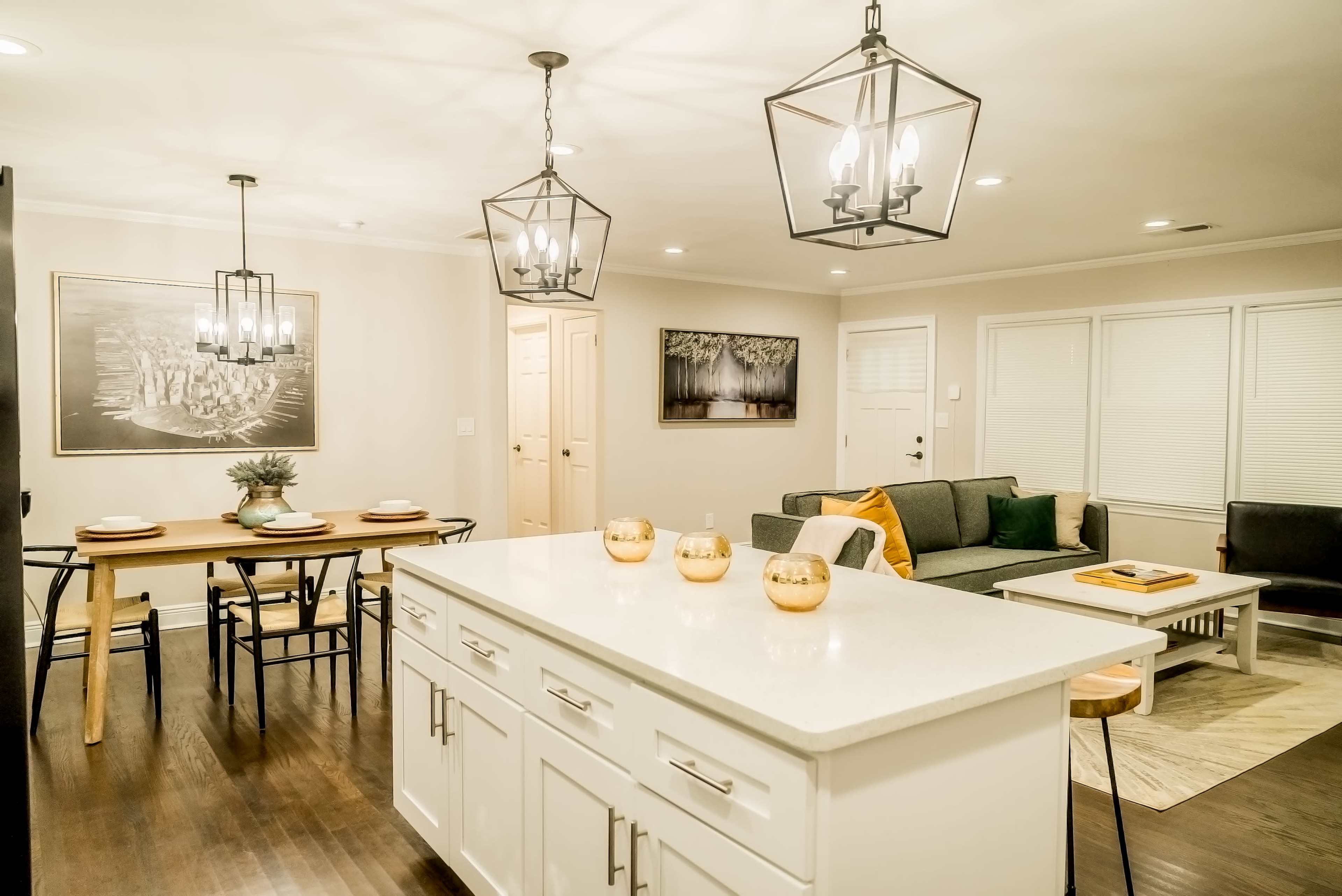 A modern living space featuring a kitchen island with bar seating, a dining area with a wooden table, and a cozy lounge area with a gray sofa.