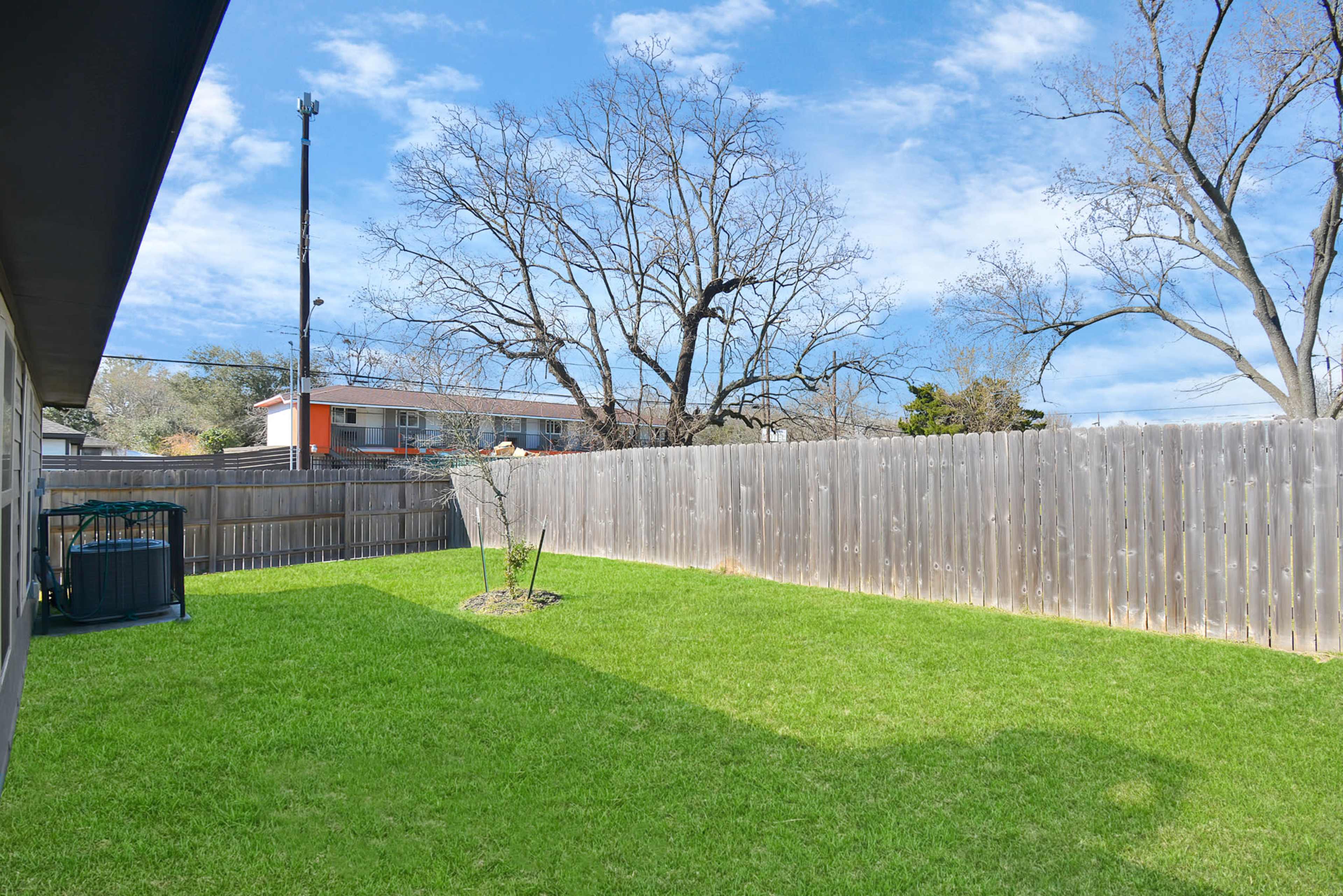 The image shows a grassy backyard enclosed by a wooden fence, with a small tree and a storage unit in one corner.