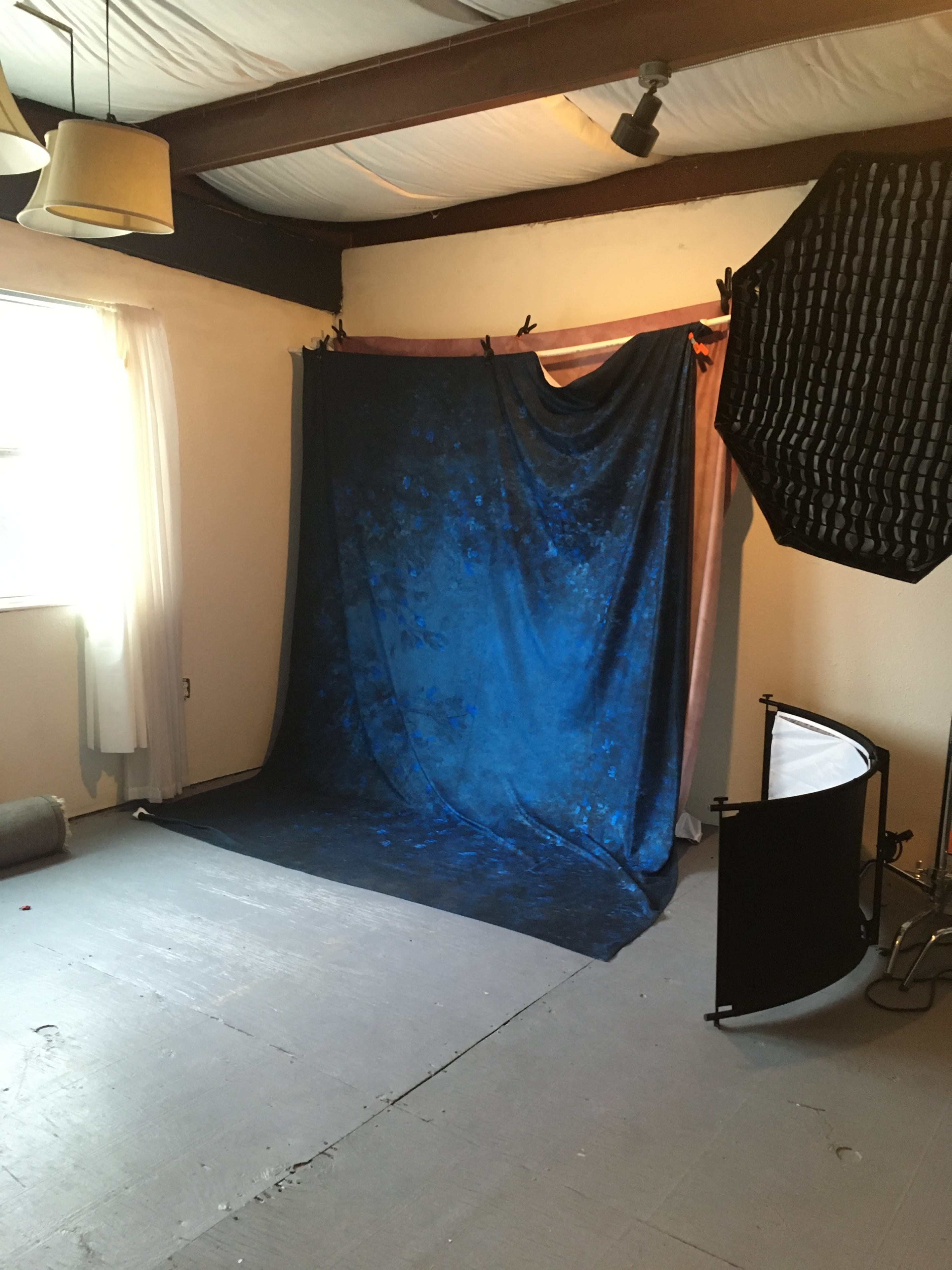 A photography studio setup featuring a blue backdrop, soft lighting equipment, and a light reflector.