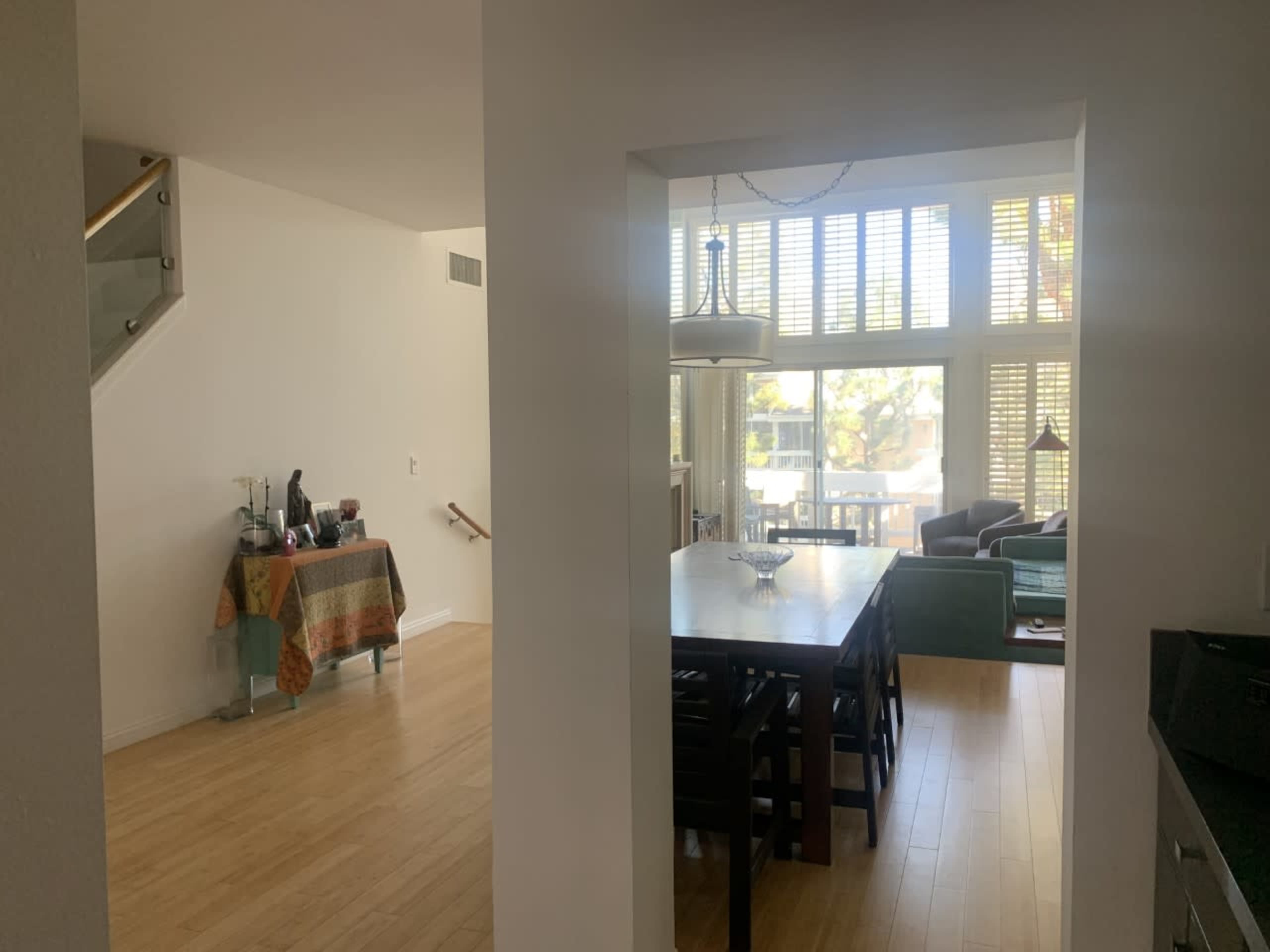 An open-concept living and dining area with a dining table, a window wall allowing natural light, and a staircase in the background.