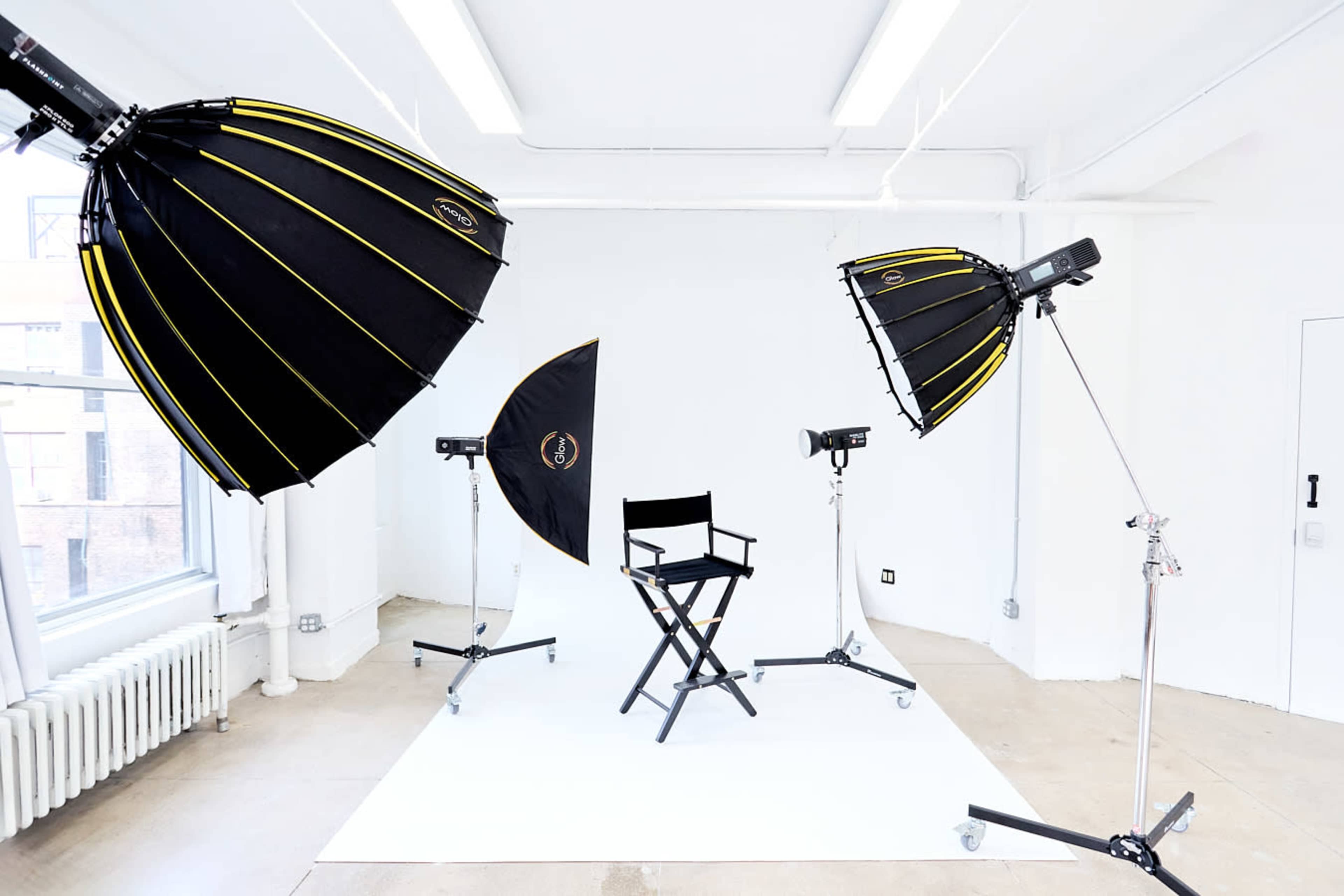 The image features a photo studio setup with two large softbox lights, a reflector, and a director's chair on a white backdrop.
