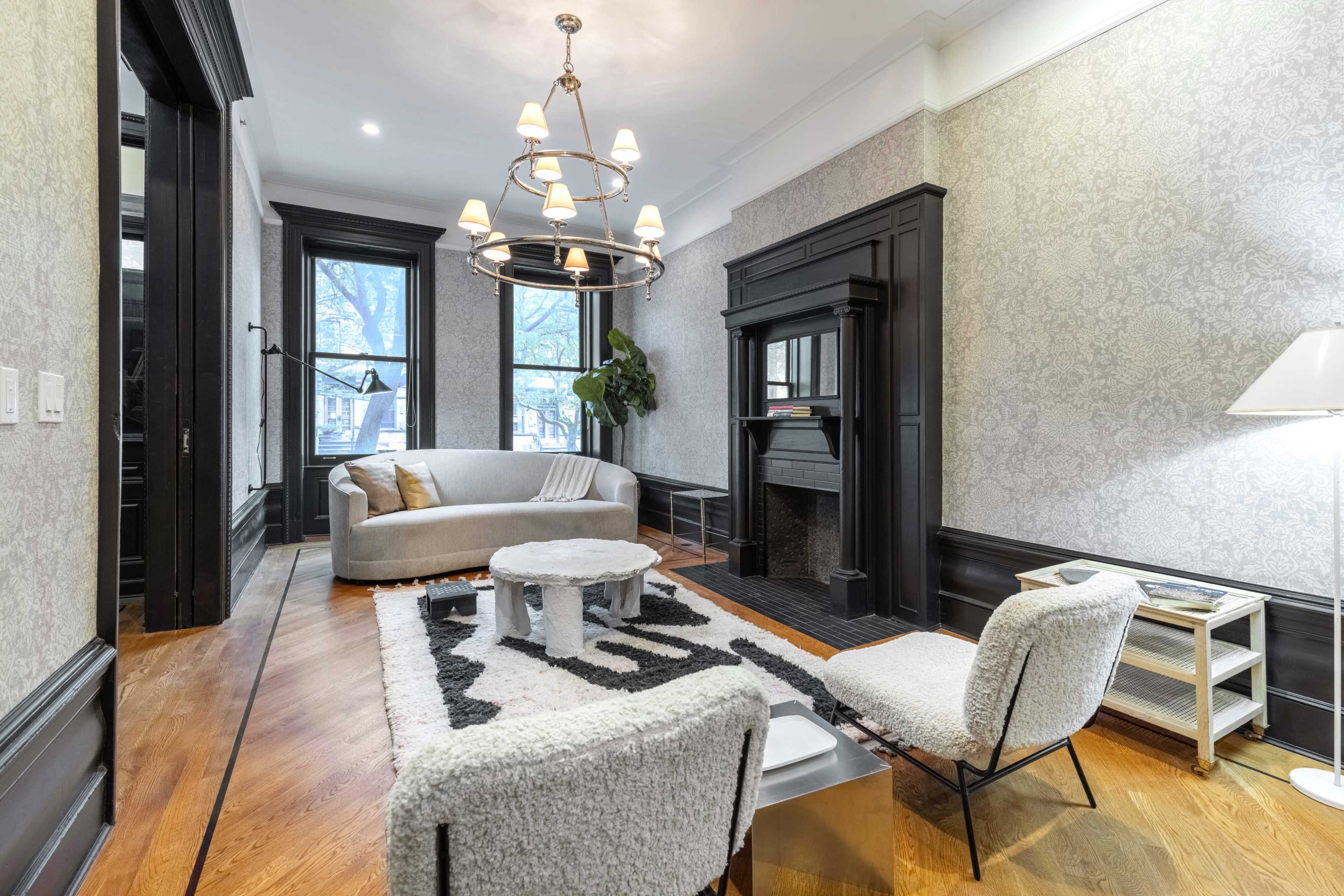 A living room with a light-colored sofa, a round coffee table, two white armchairs, and a decorative fireplace against a patterned wall.