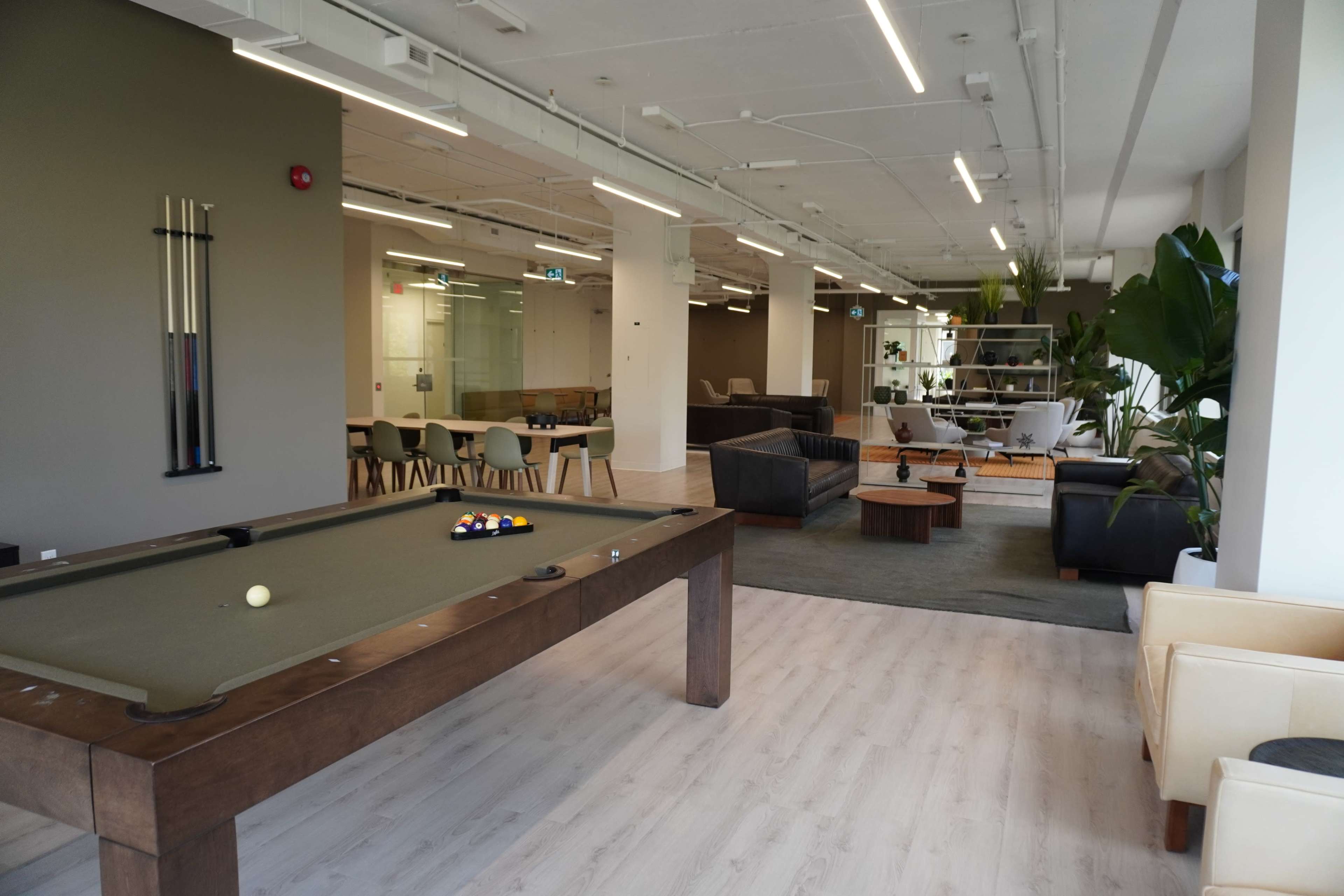 The image shows a spacious lounge area with a pool table, modern furniture, and a mix of seating arrangements in a well-lit room.