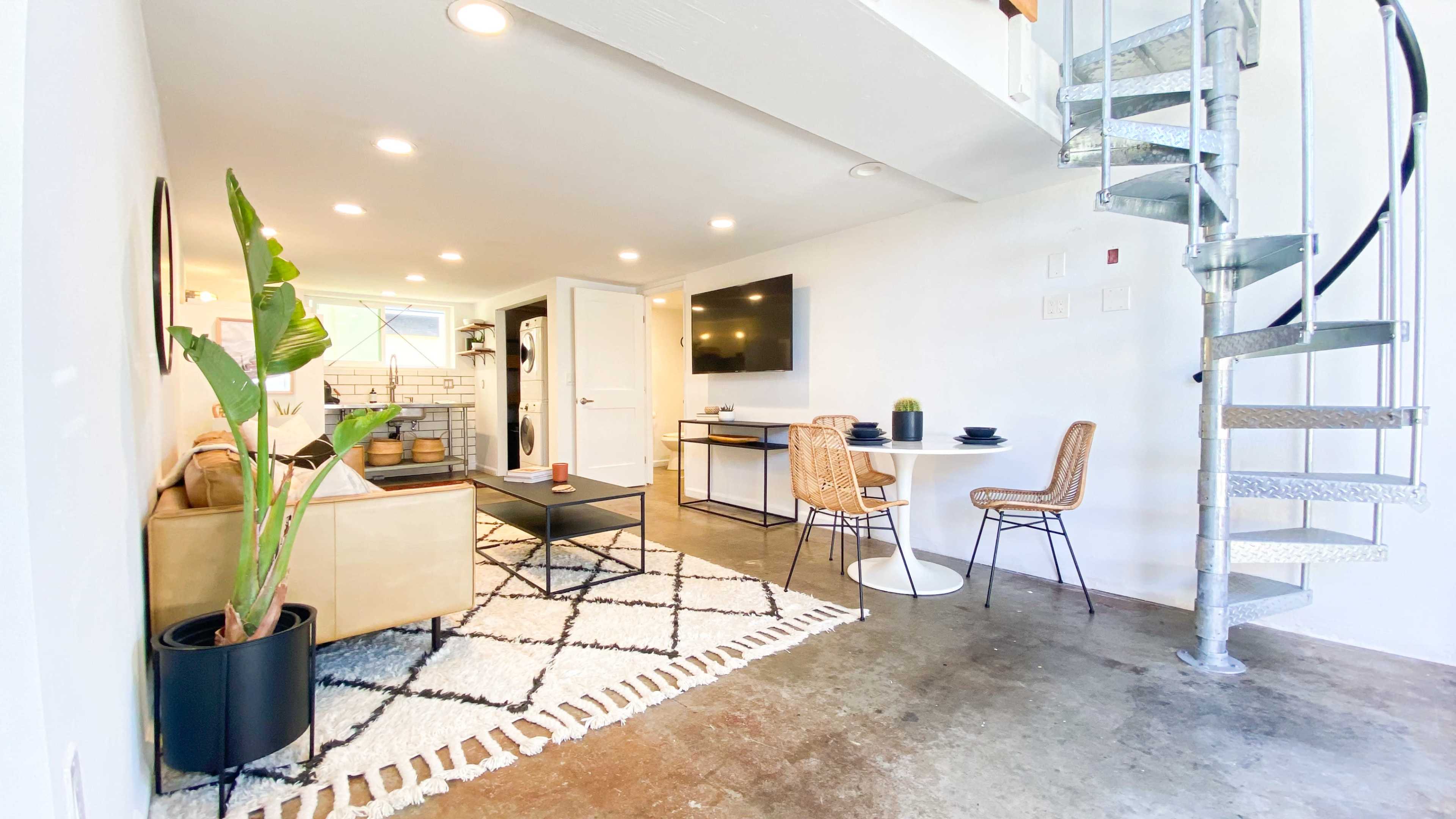 A modern living space featuring a spiral staircase, a seating area with a couch and coffee table, a dining area with two chairs, and a kitchen visible in the background.