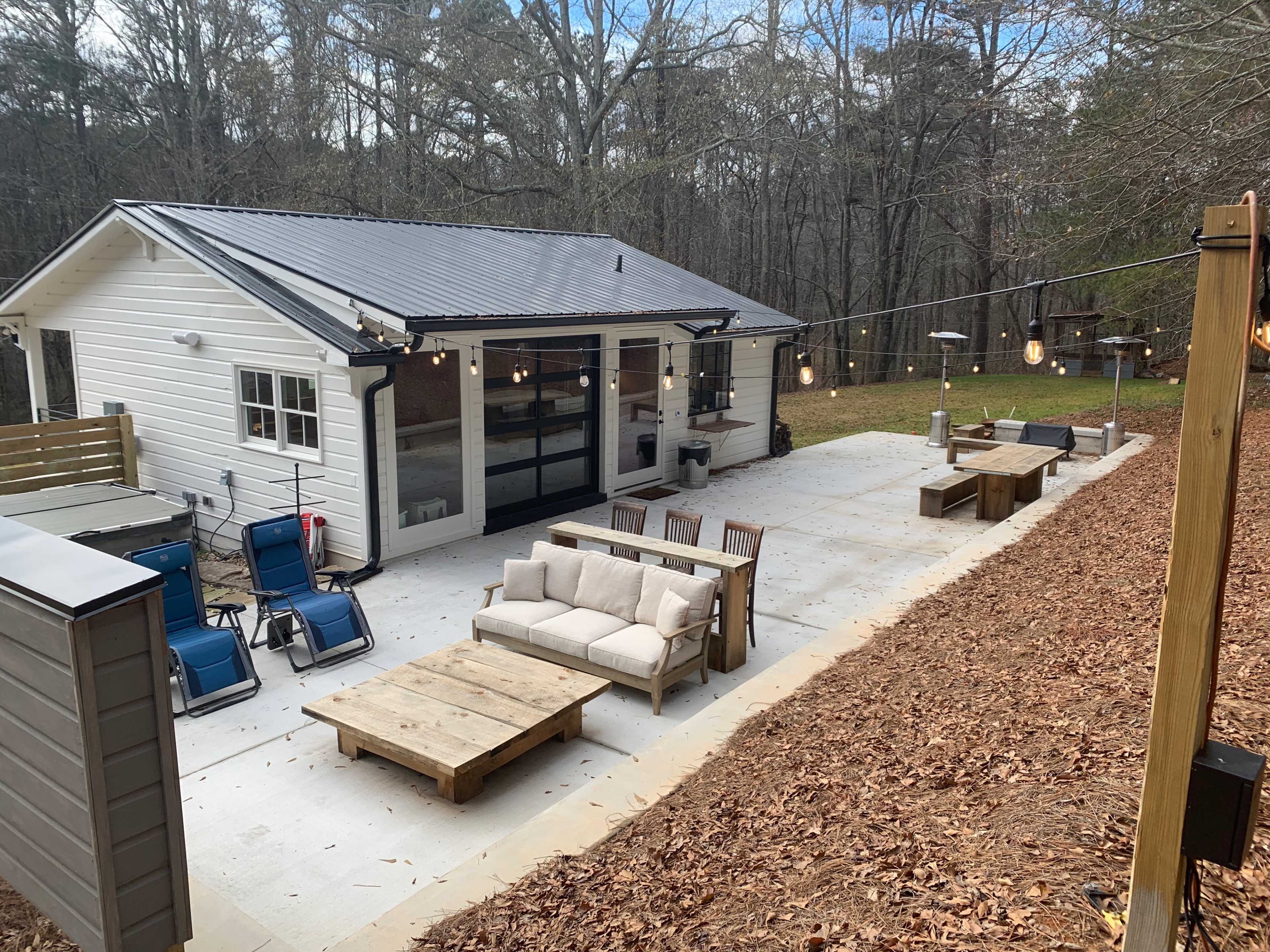 A backyard area features a modern cabin, outdoor seating with a coffee table, and string lights illuminating the space.