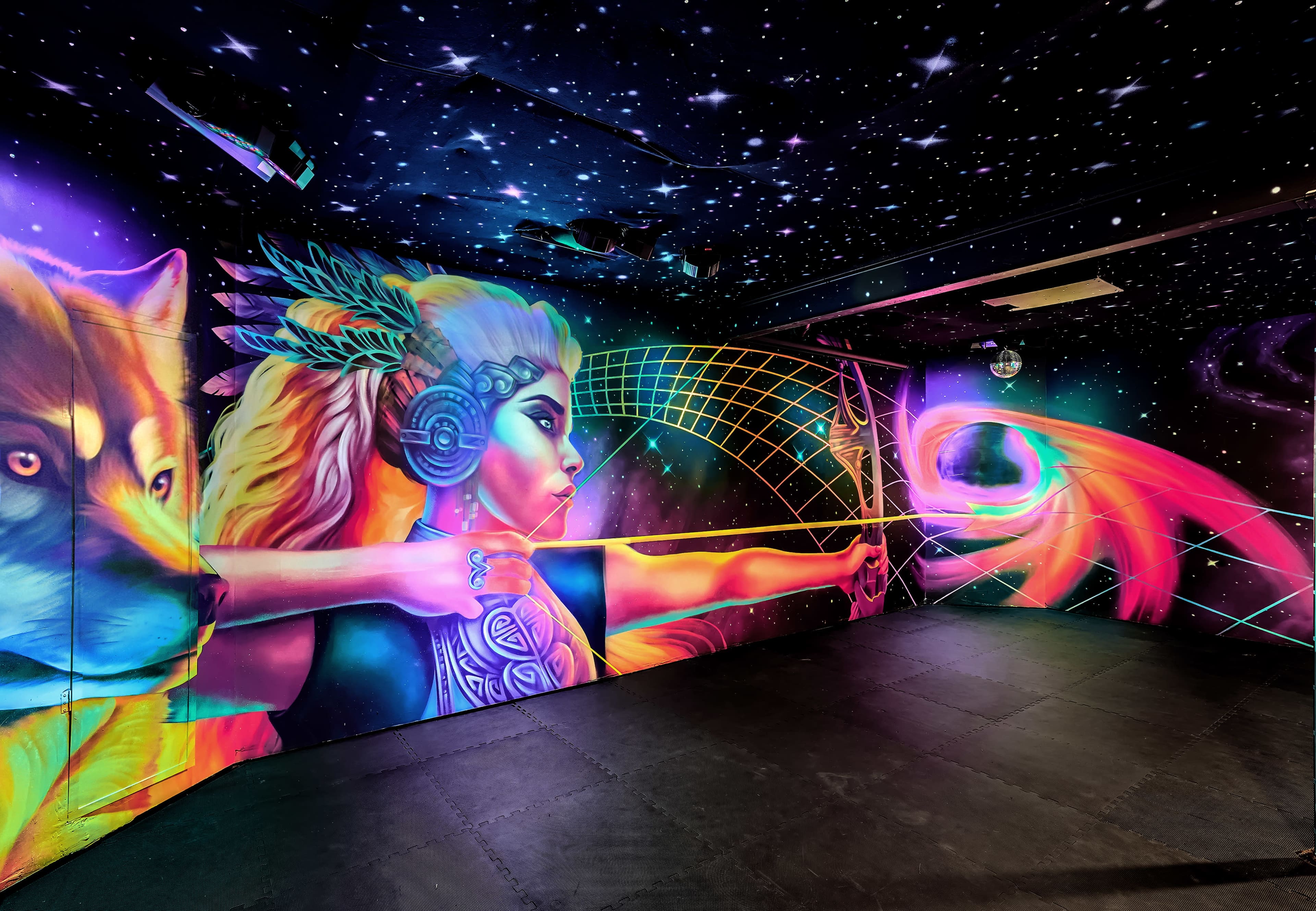 A room with vibrant, colorful mural art on the walls, depicting a woman and a wolf against a cosmic background filled with stars.