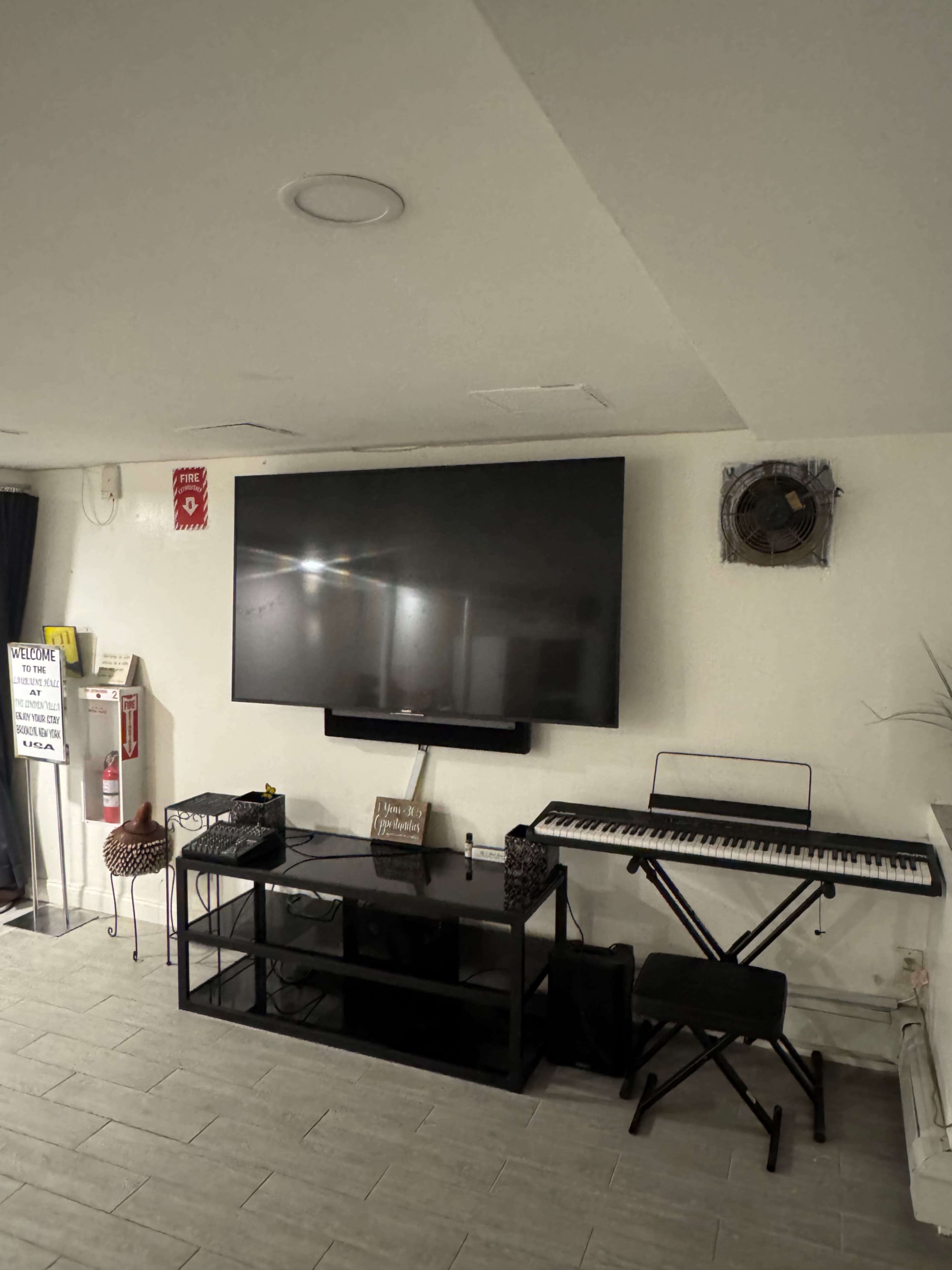 The image shows a basement room with a large wall-mounted television above a black media console and a keyboard on a stand.