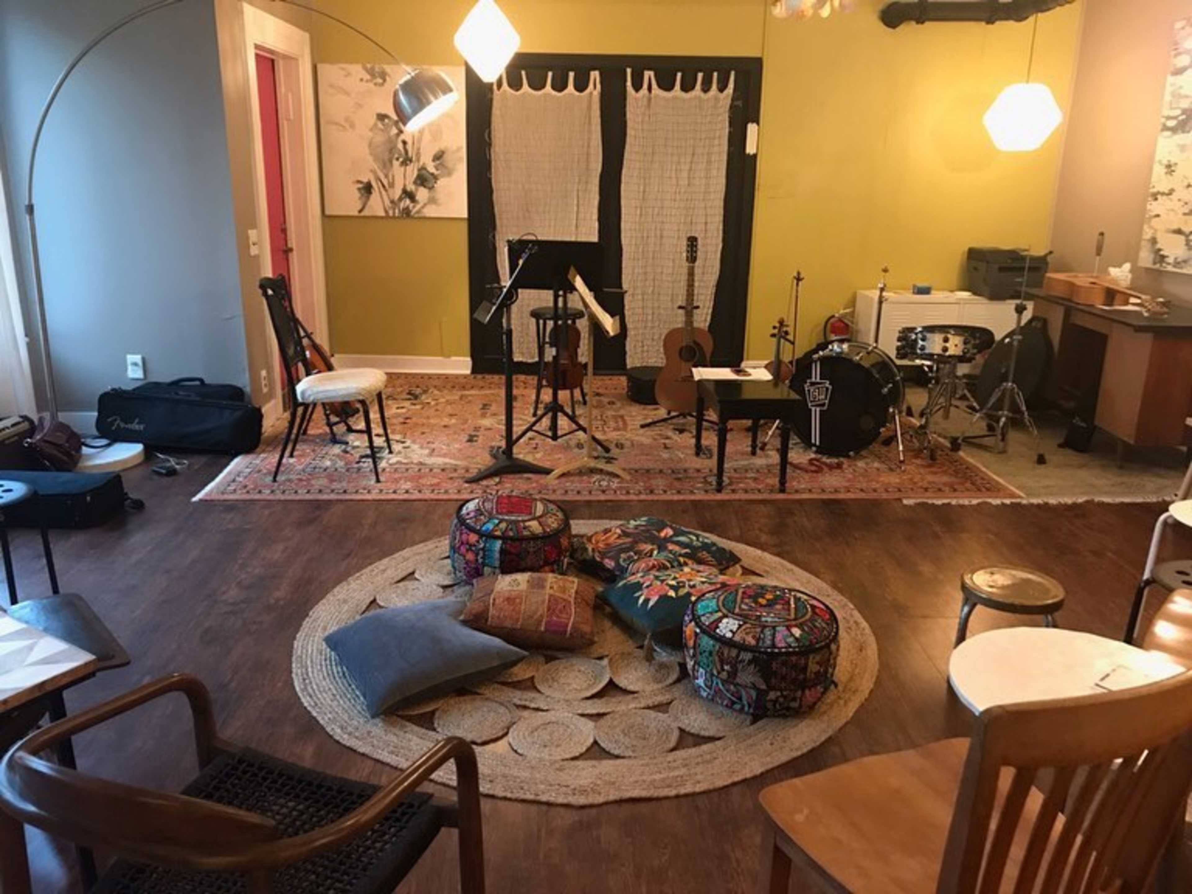 A cozy room set up for music practice, featuring chairs, instruments, and colorful poufs arranged around a circular rug.