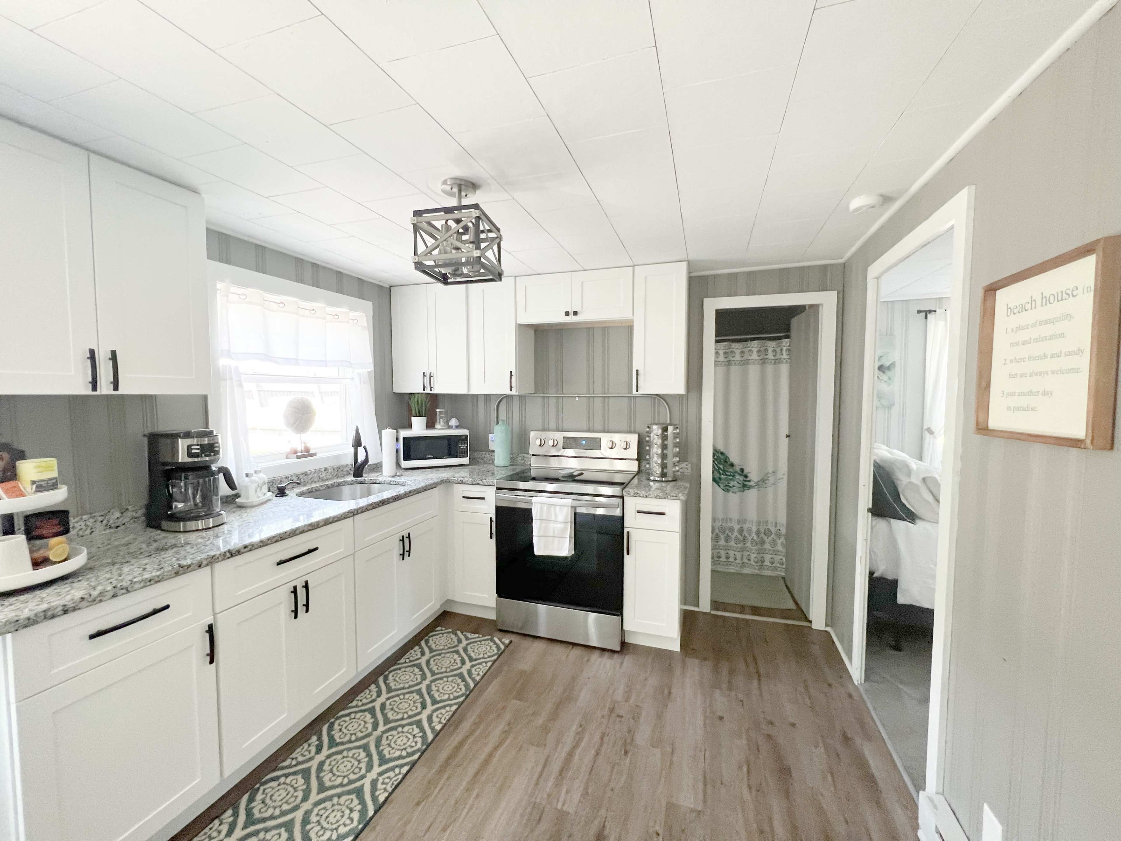A modern kitchen featuring white cabinetry, a stainless steel stove, and a patterned mat on the floor.