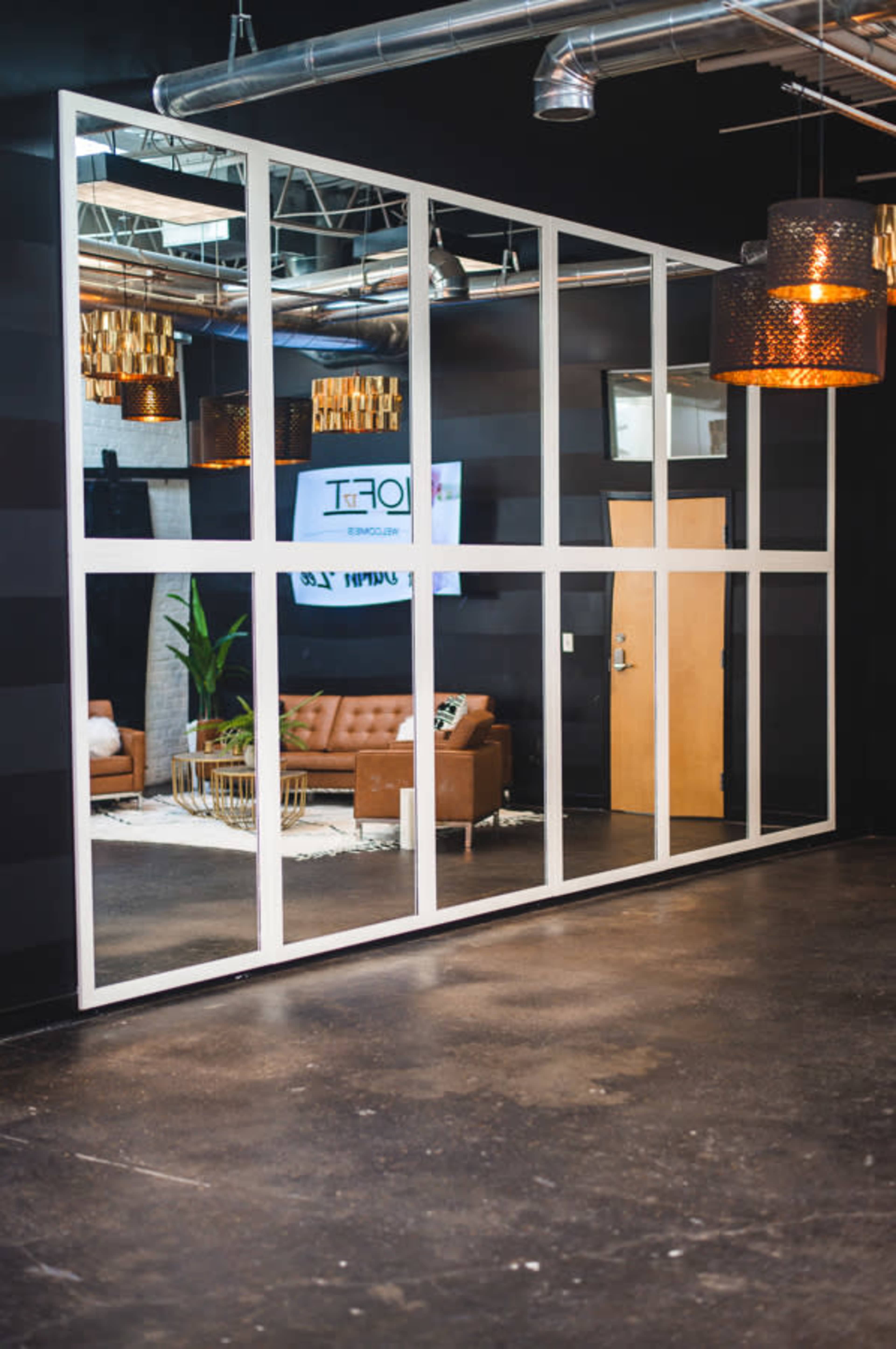 The image shows a large mirror wall in a room with dark walls, featuring a modern seating area and decorative lighting.