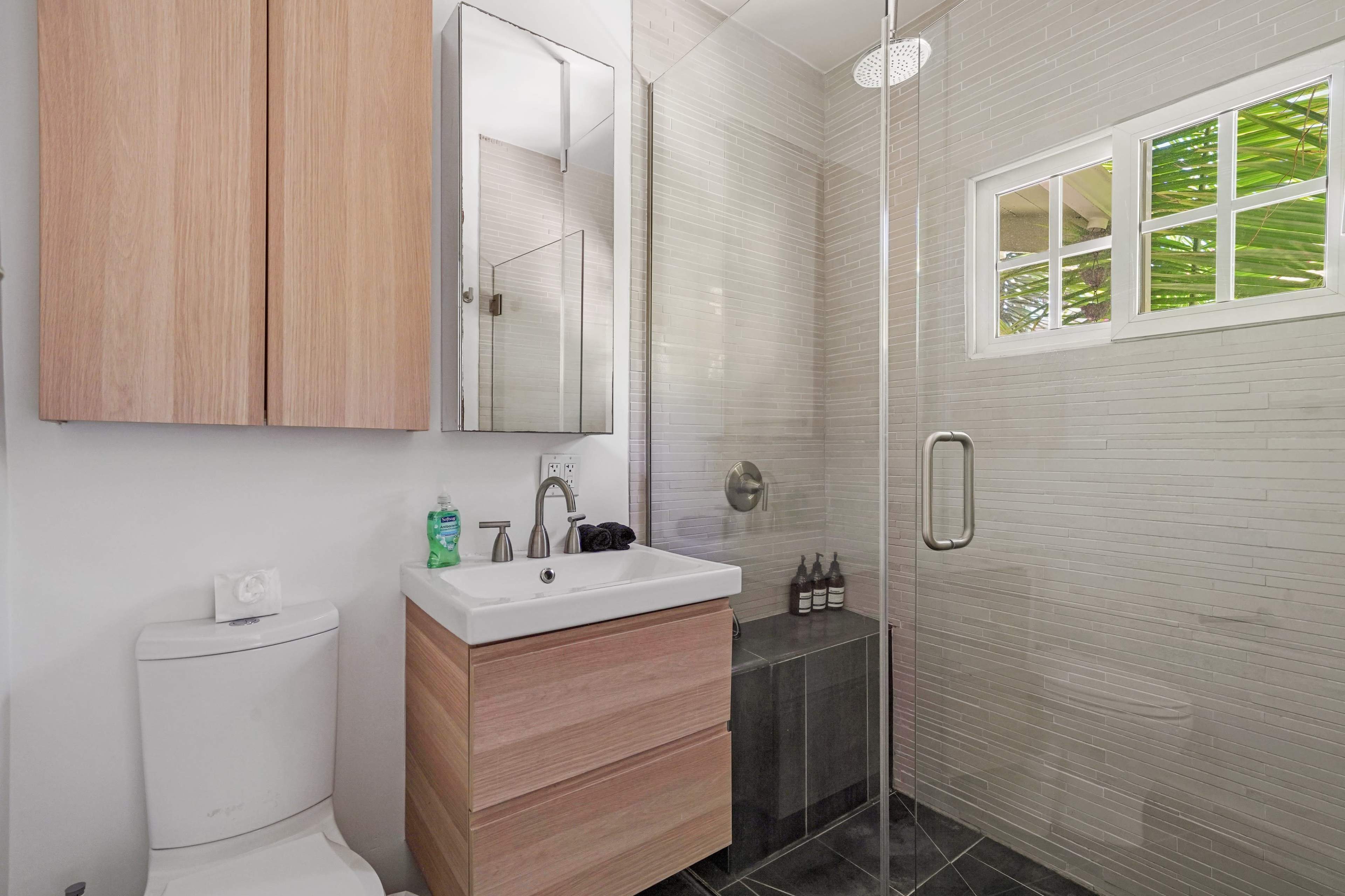 The image shows a modern bathroom featuring a shower with glass doors, a wooden vanity with a sink, and a wall-mounted mirror.