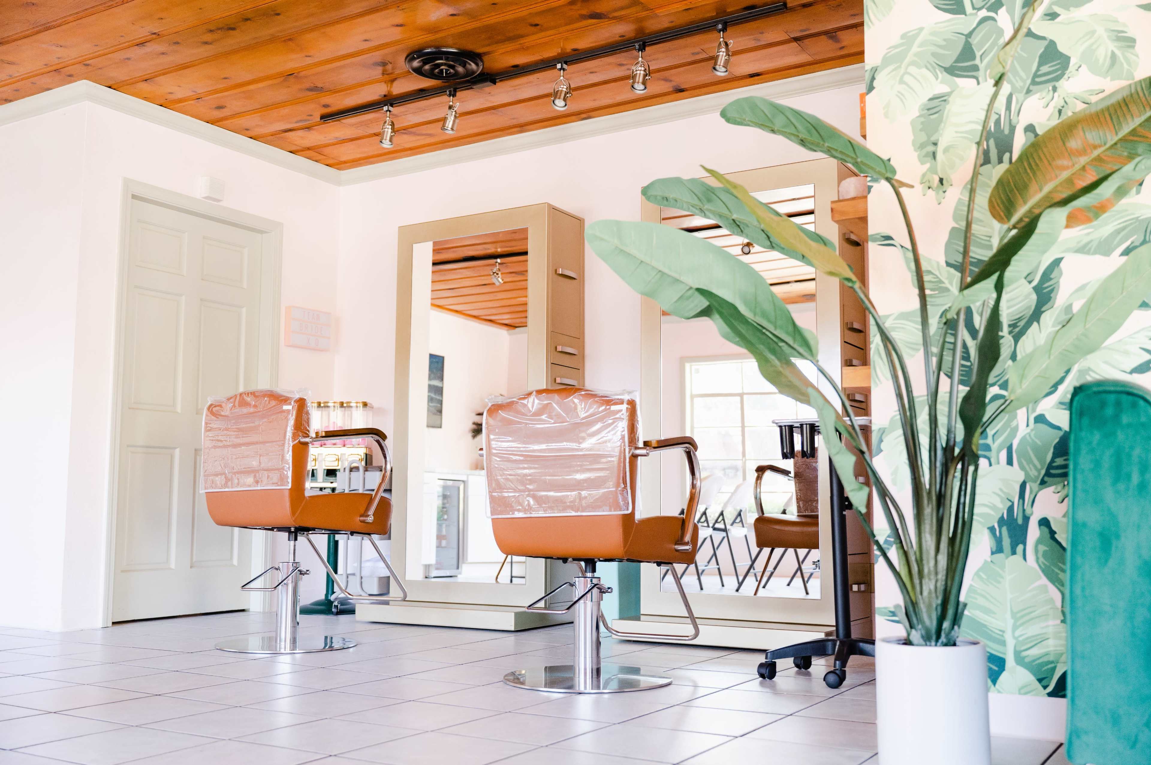 A modern hair salon interior with two styling chairs, large mirrors, and decorative plant life.